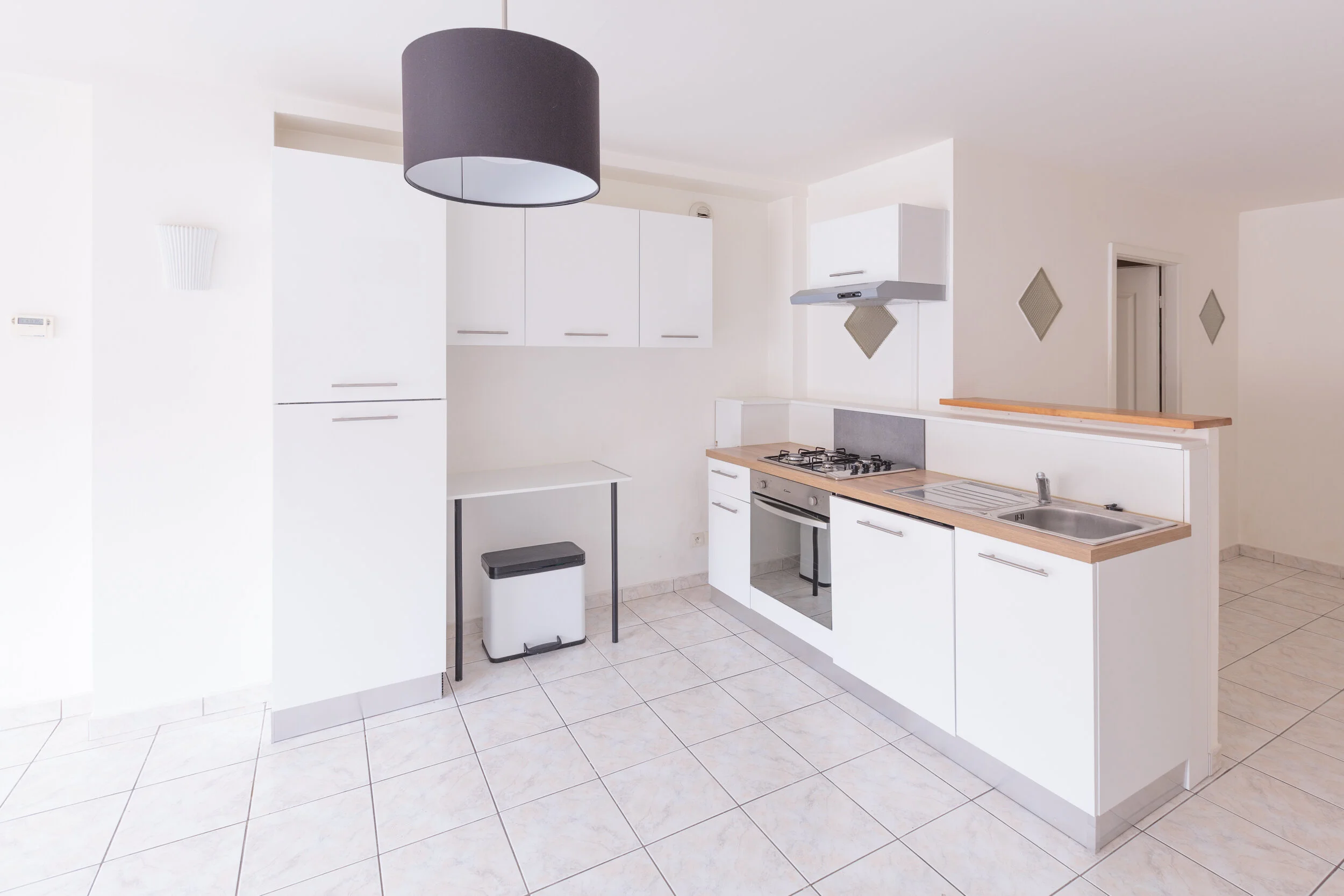 Empty modern kitchen with white cabinets, a black ceiling fan, a small table, and a tile floor.