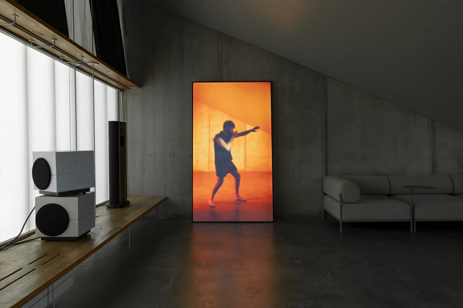 Modern living room with a digital artwork of a dancer in orange lighting, a white couch, large speakers, and a wooden shelf with audio equipment.