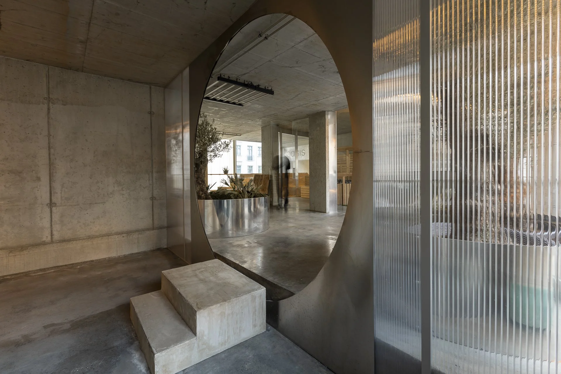 Modern interior with concrete walls, a circular opening, stairs, and a person walking in the background.