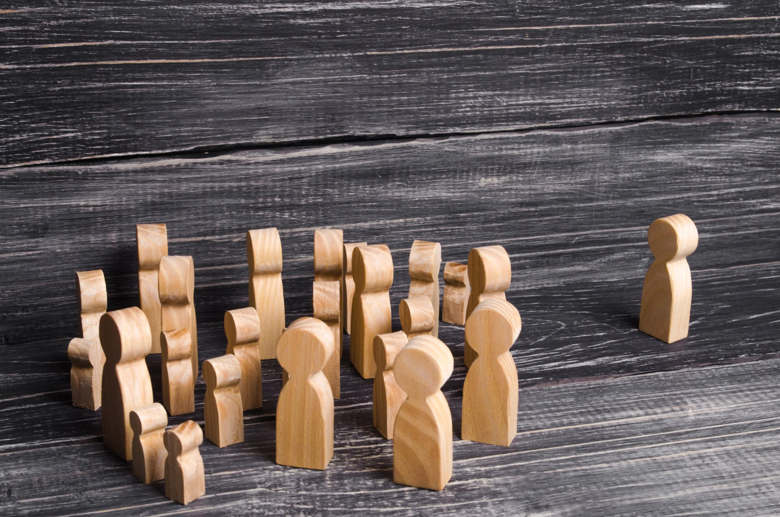 wooden figures in a crowd, with one standing outside the group