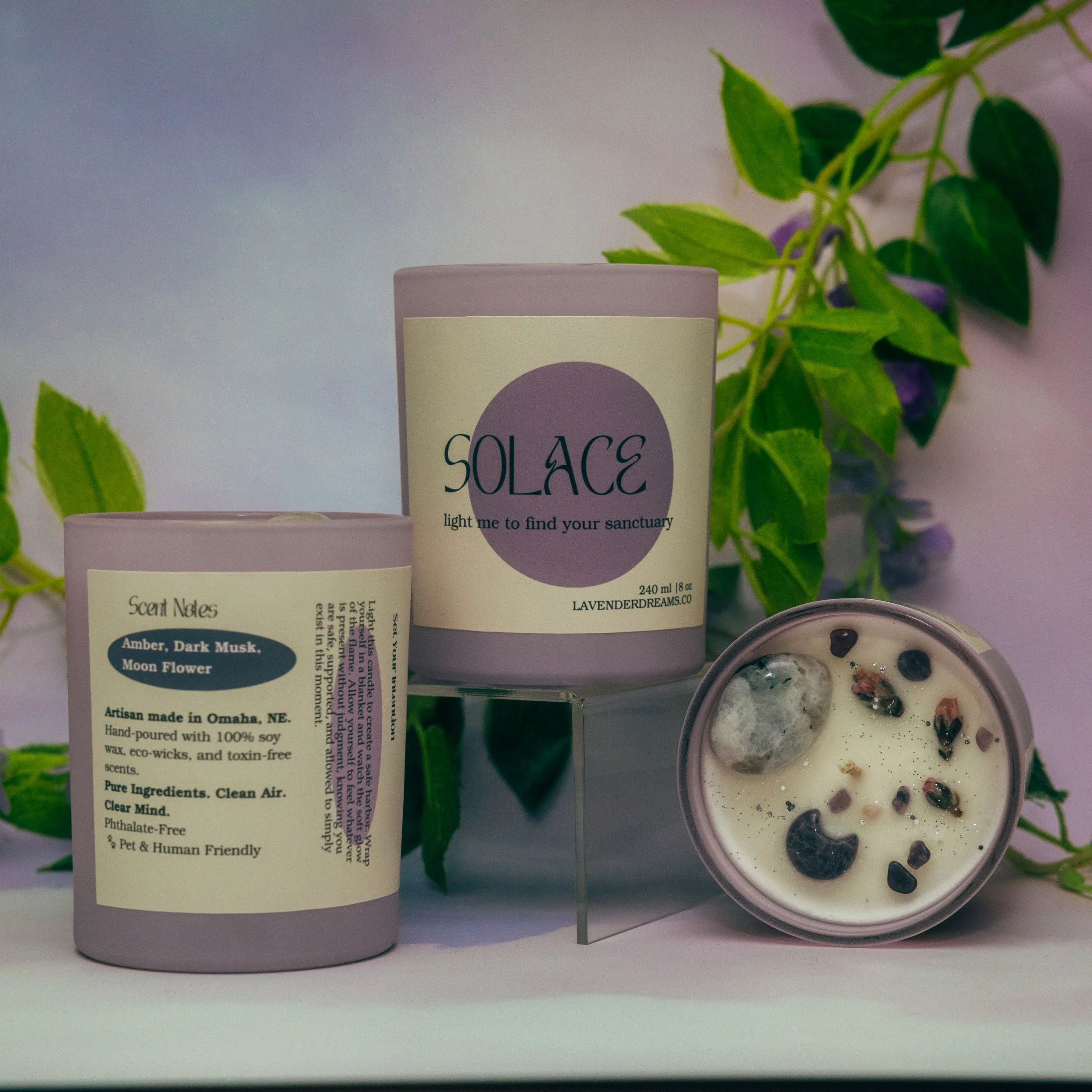Close-up of a pink container labeled 'SOLACE' with a lavender circle, next to another pink container, plants in the background, and a bowl of yogurt with berries.