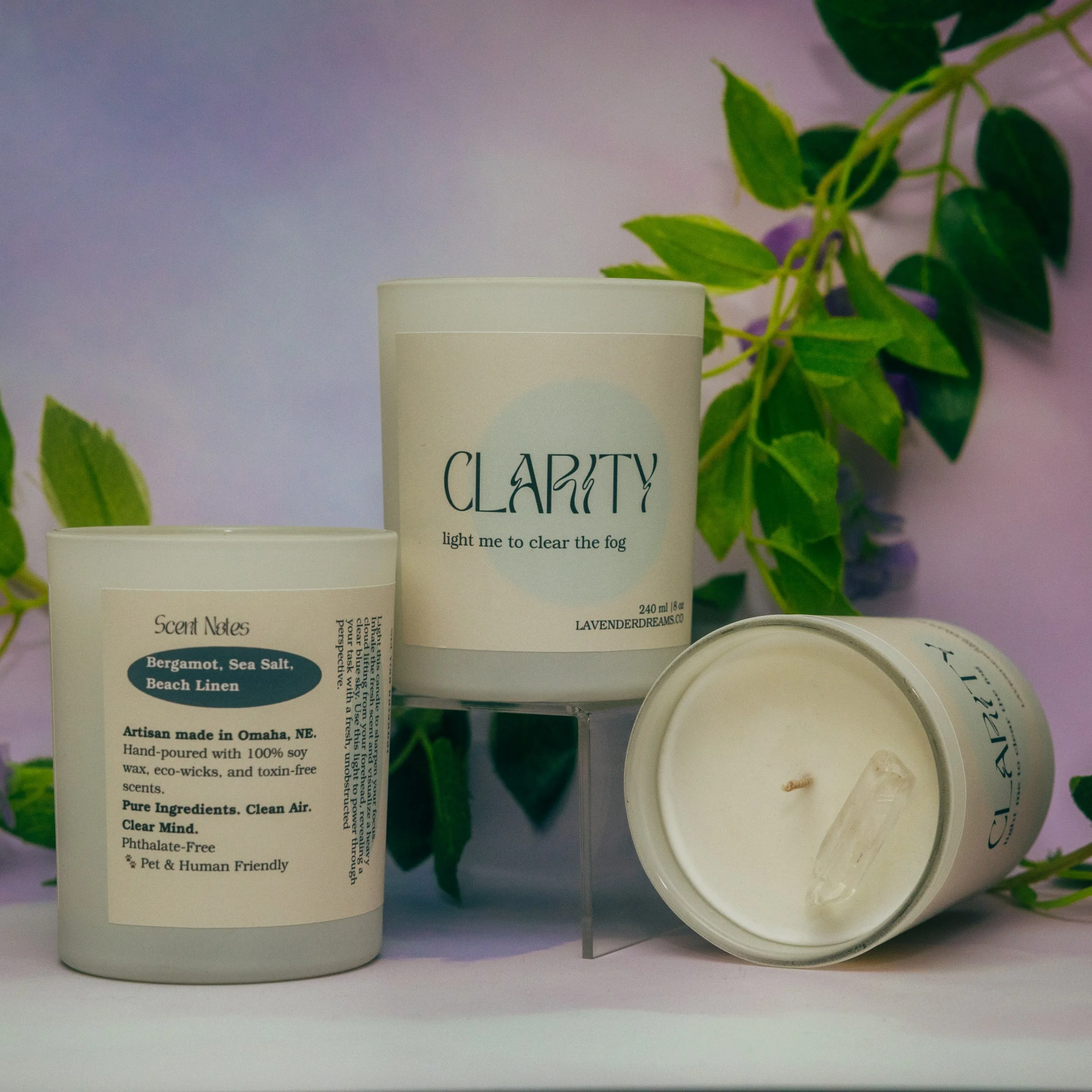 A white cylindrical container labeled 'Clarify' with text 'light me to clear the fog' and a white lid, alongside another cylindrical container with a partially visible label reading 'Scent Notes,' and a small white bowl filled with a white substance,