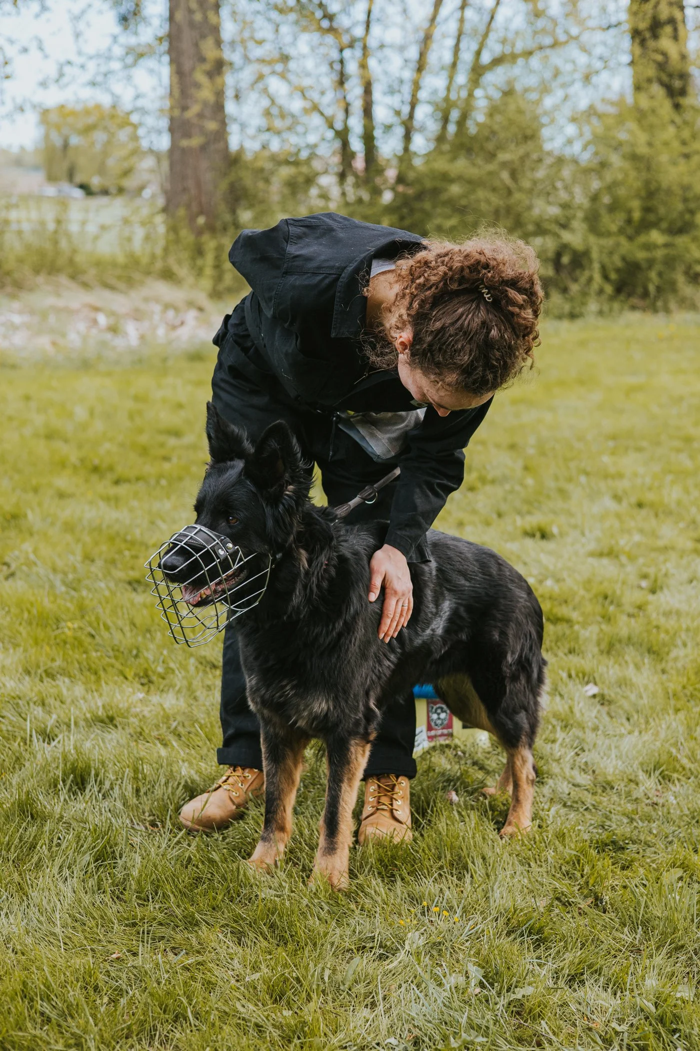 Eine Frau beugt sich über ihre Schäferhündin und streichelt ihr liebevoll über die Seite. Der Hund schaut gespannt in die Ferne.