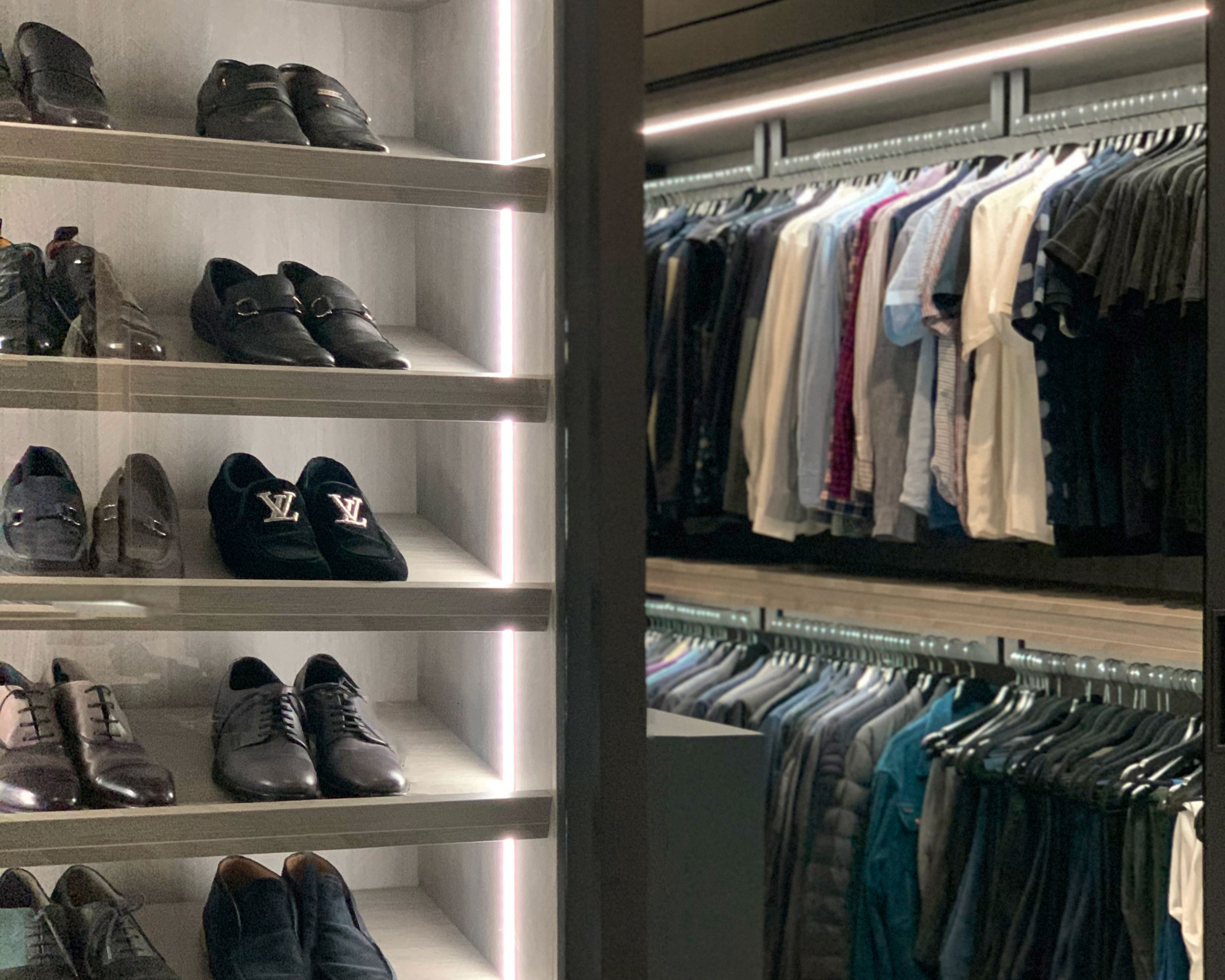 Display of men's dress shoes on shelves and hanging clothes in a wardrobe.