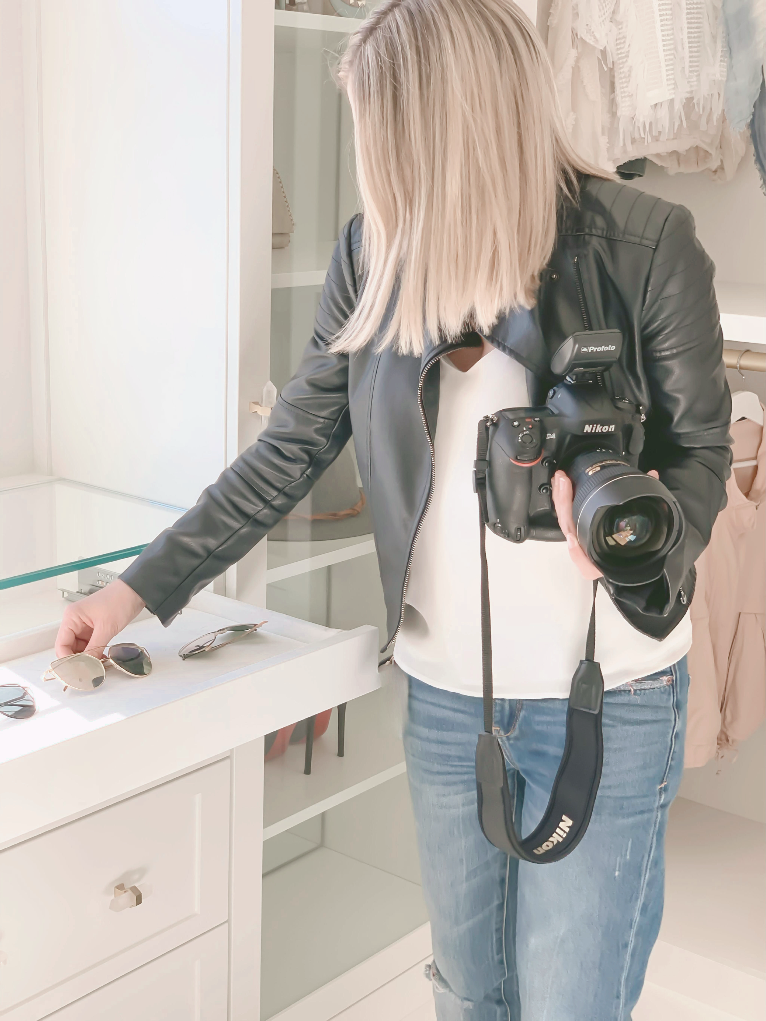 A woman trying on sunglasses at a store, holding a camera.