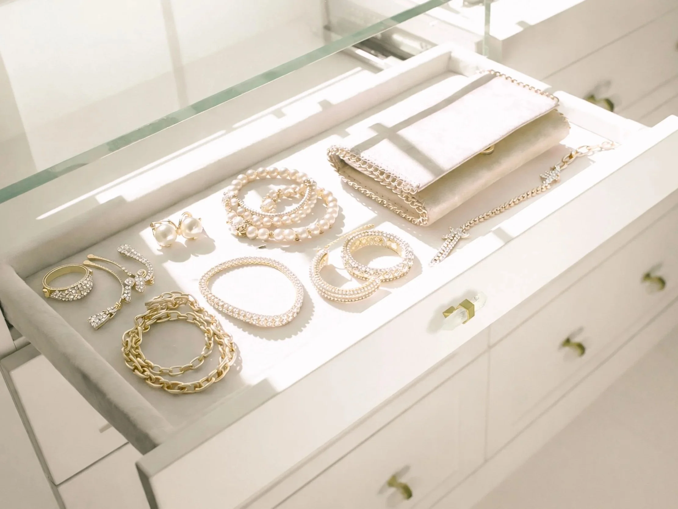 Jewelry including rings, necklaces, earrings, and bracelets displayed on a white tray inside a glass display case.