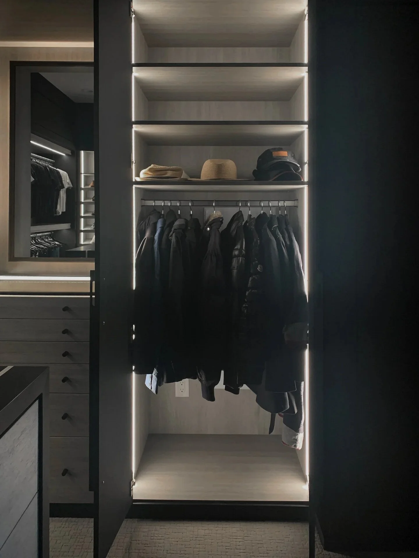 A modern walk-in closet with built-in shelves and hanging space for jackets and hats, illuminated by LED strip lighting.