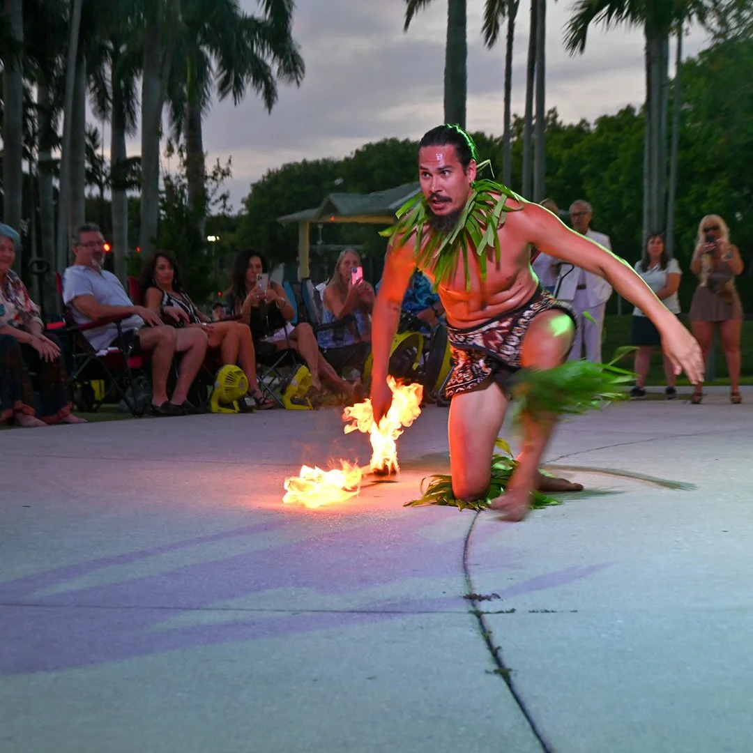 A performer wearing traditional attire performs a fire dance in front of a crowd at the Wellington Amphitheater.