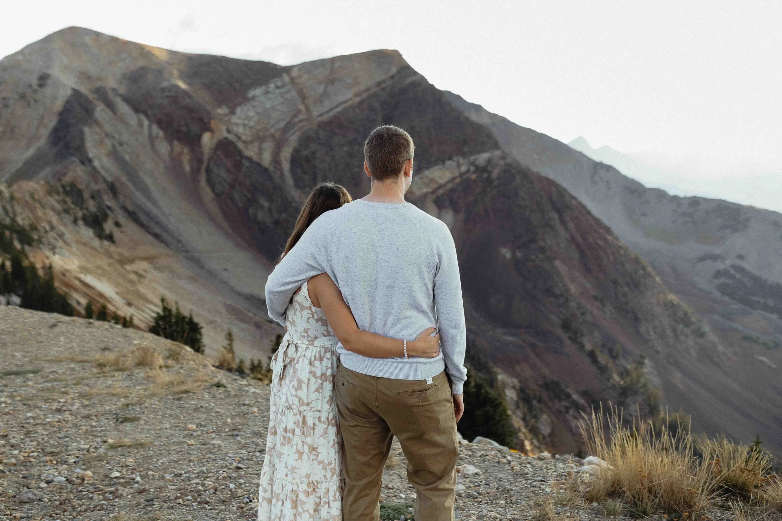 Couple embracing in front of rocky mountain in the background.