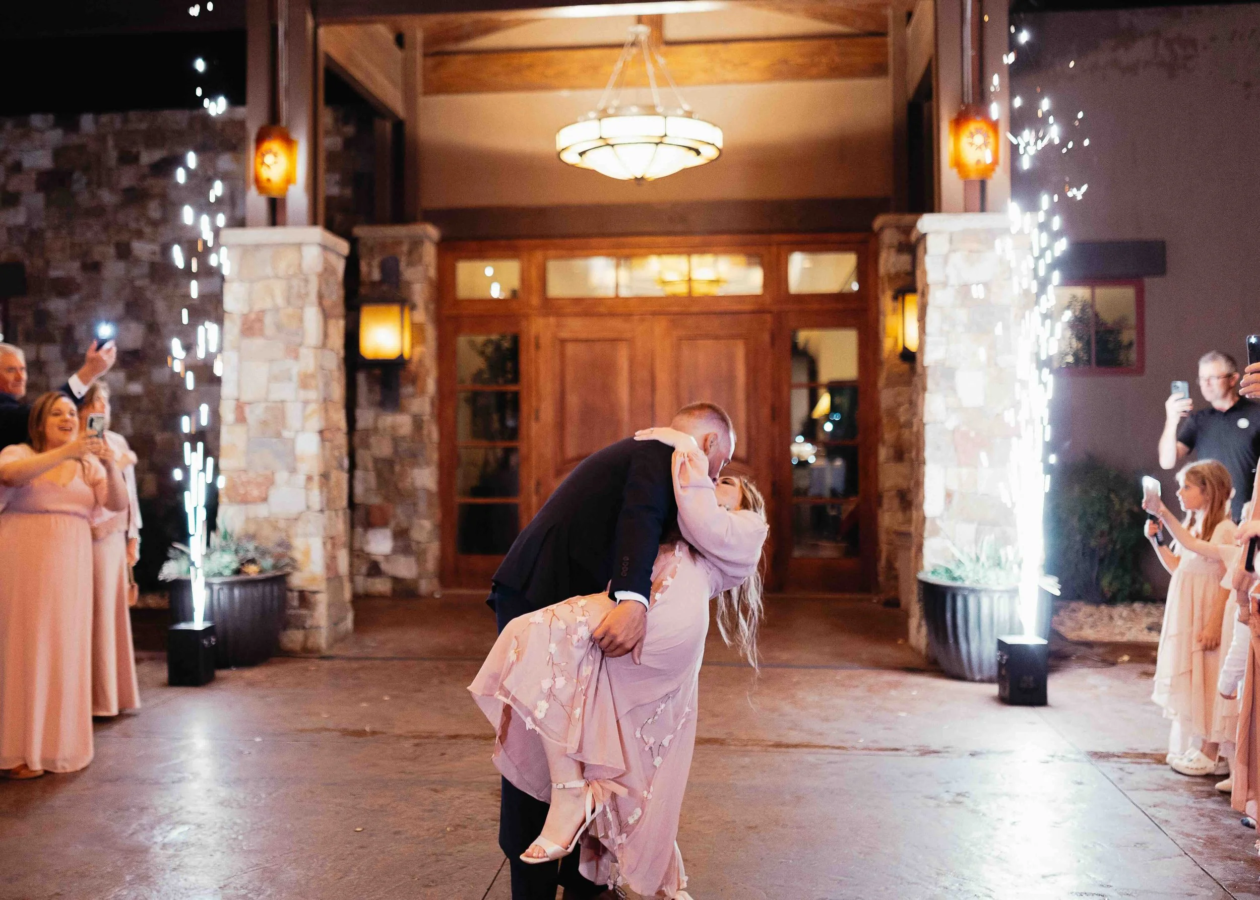 Couple kissing on their wedding day exit with sparkler boxes going off in the background.