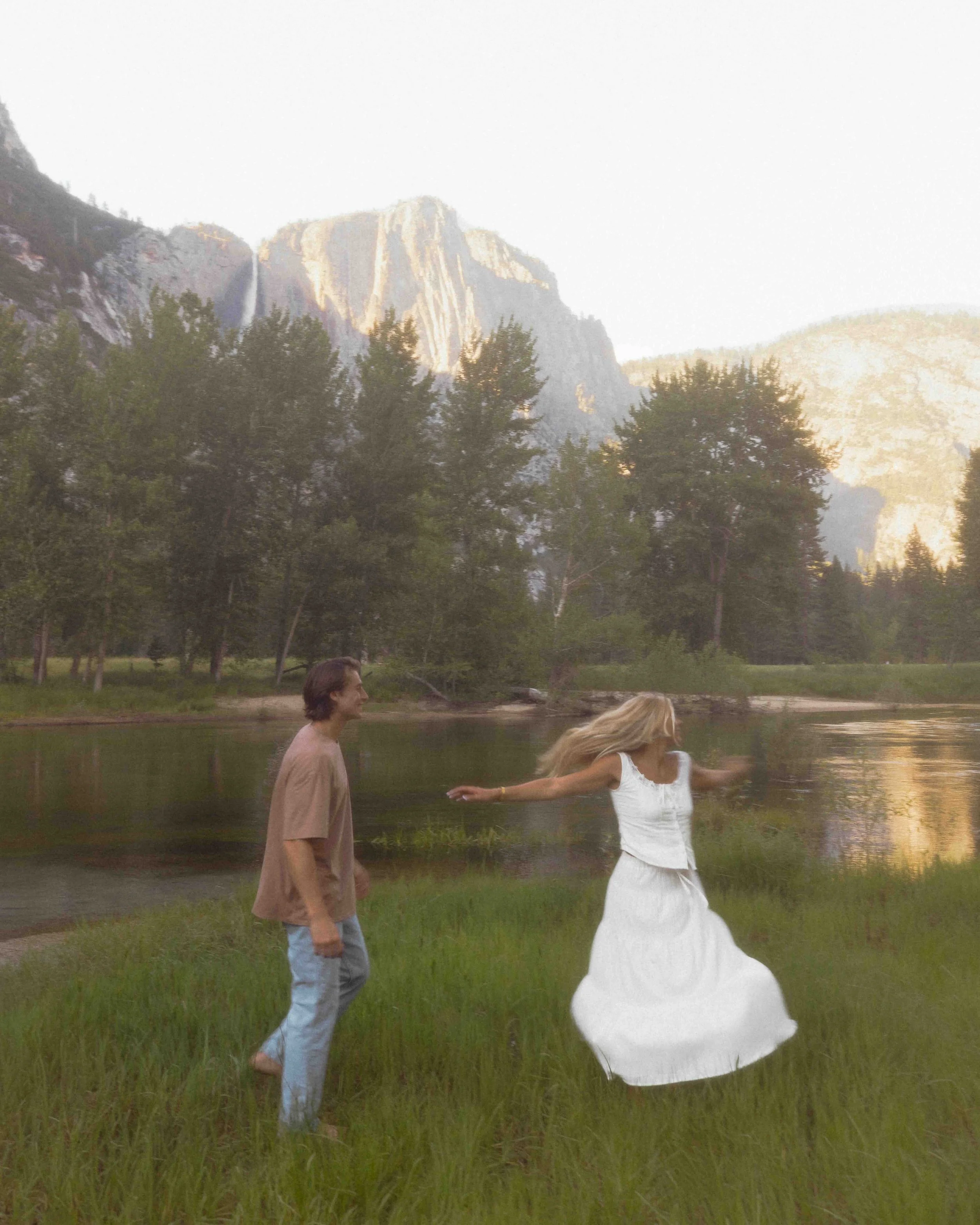 Image of recently engaged couple spinning around in front of the Merced river and grey cliffs of Yosemite National Park.