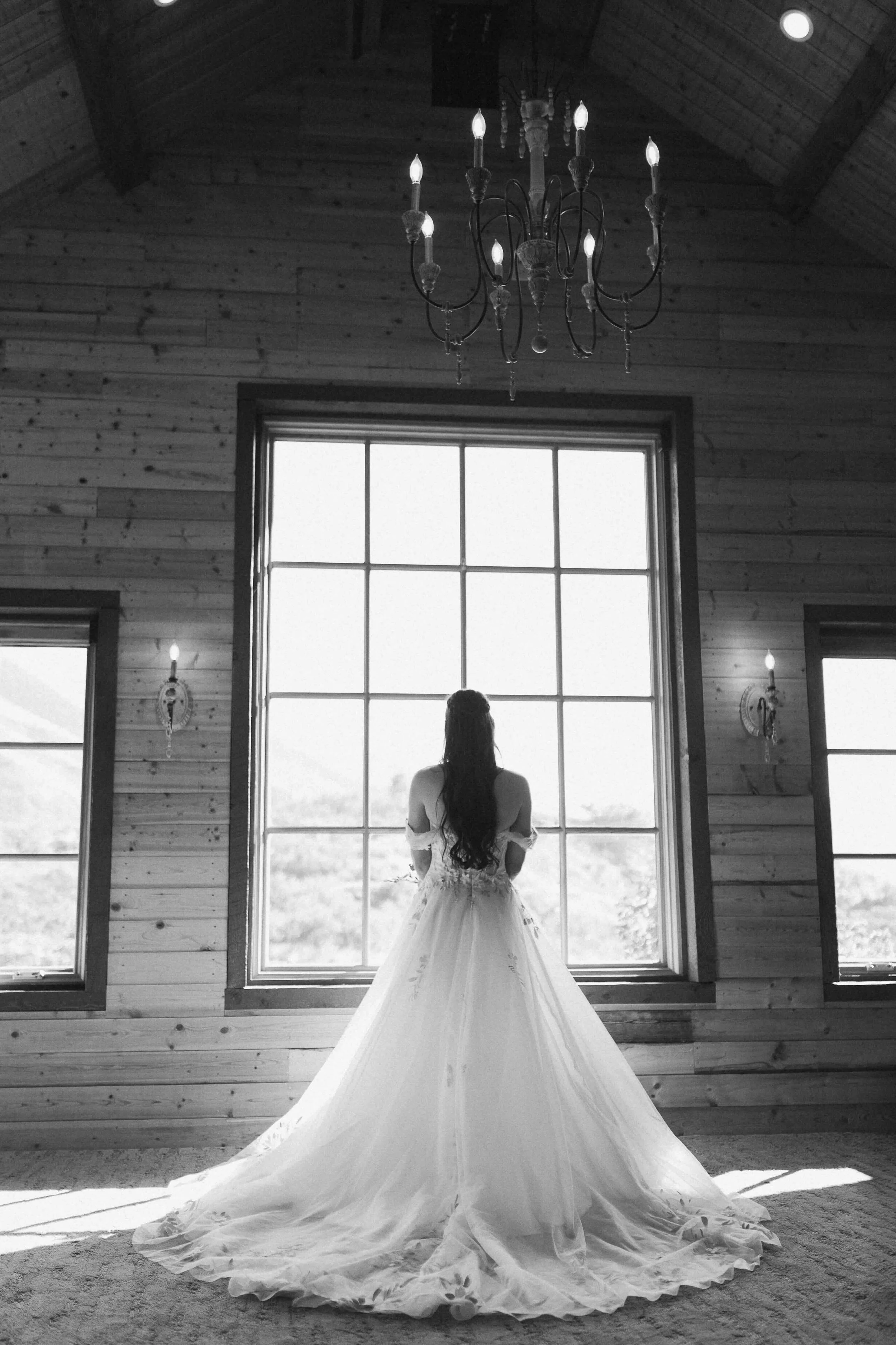 Black and white image of bride standing in front of large barn window.