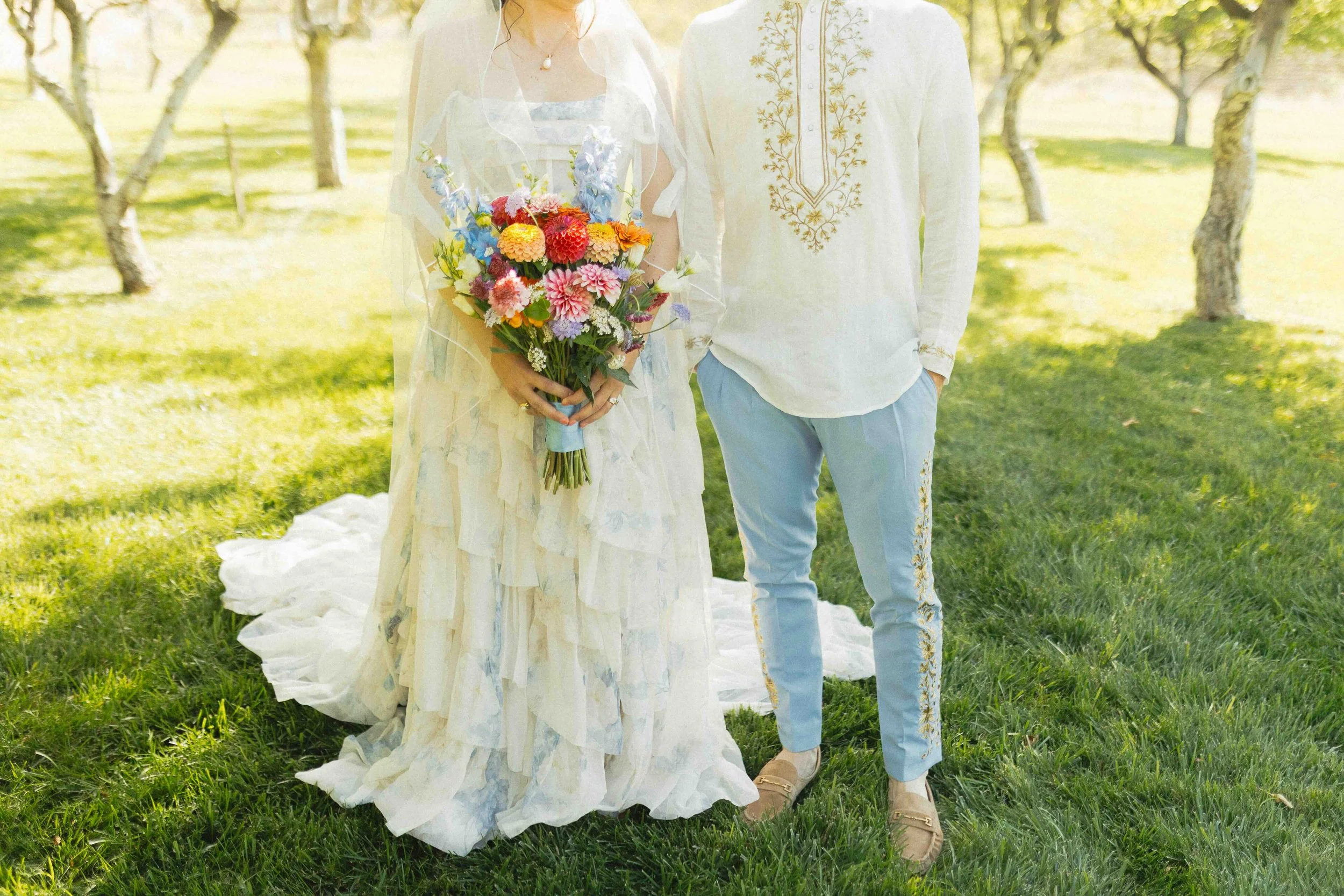 a bride and groom in unconventional wedding attire - dress with blue butterflies on it and blue linen pants with embellishments on the side for the groom.