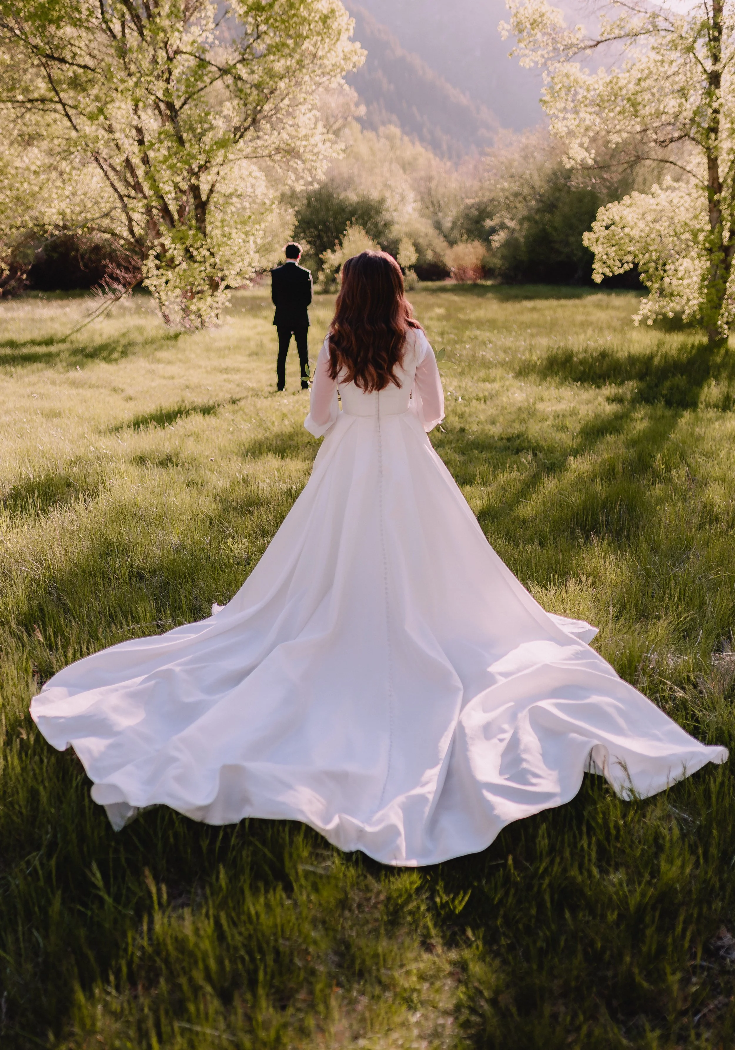 Bride approaching groom in a field with mountains for their first look