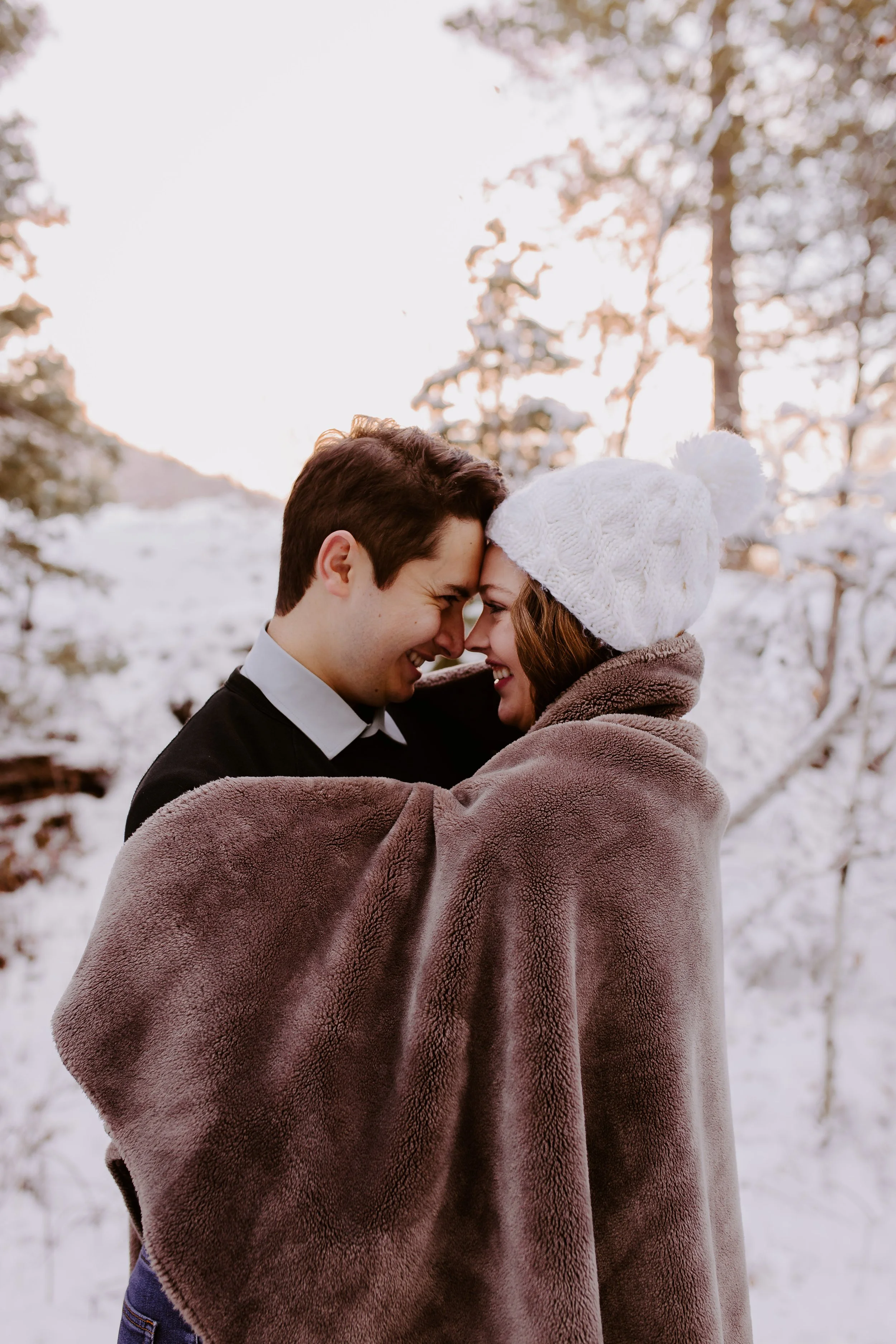 A man and woman standing wrapped in a blanket in a snowy field