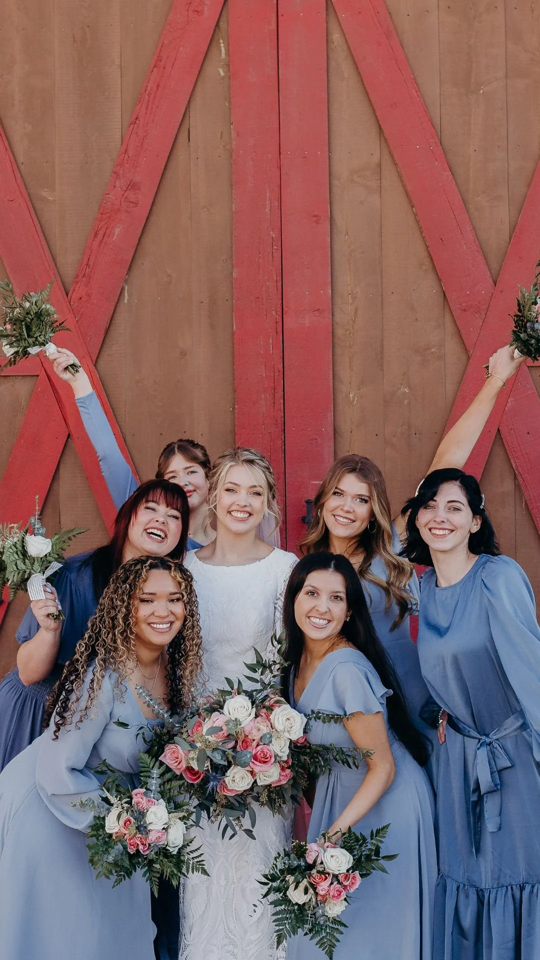 Bridesmaids in blue holding up their bouquets in front of barn doors