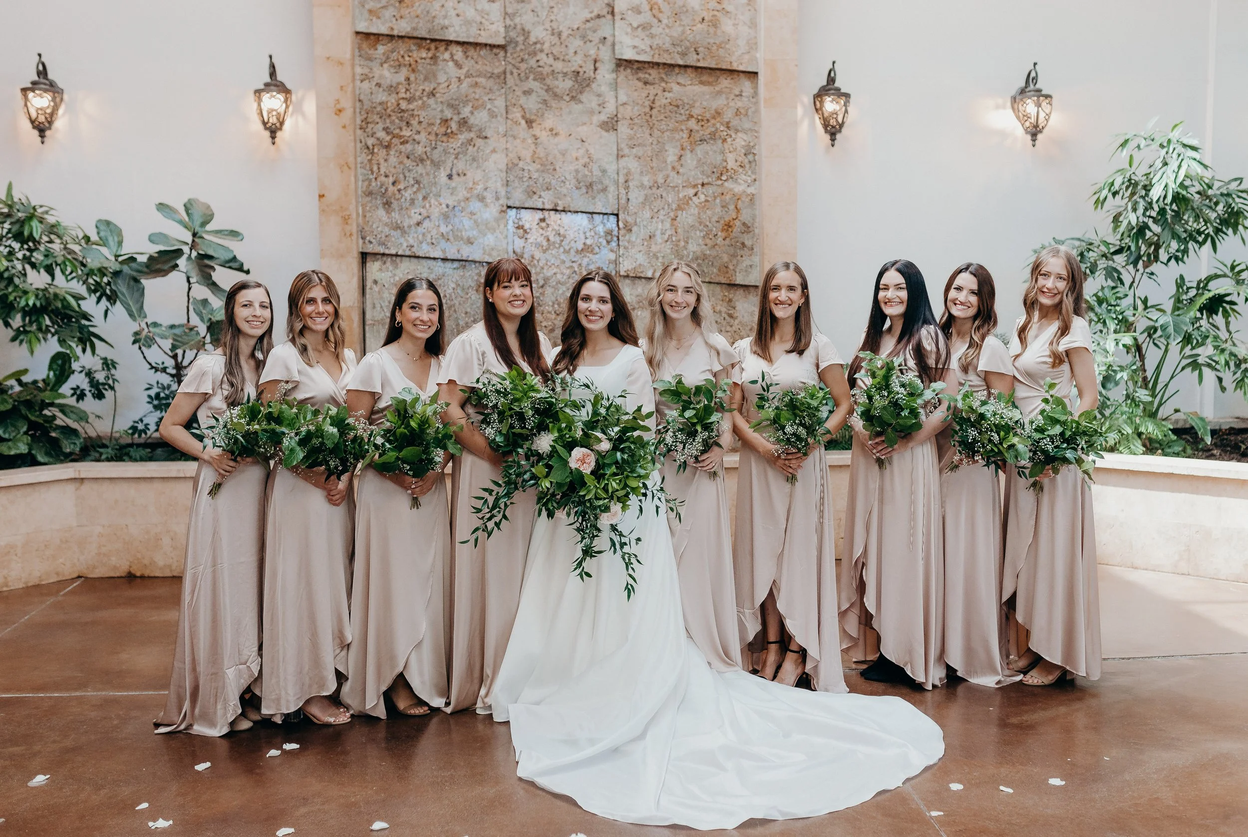 Bridesmaids in pink dresses holding onto greenery bouquets with bride in ceremony space