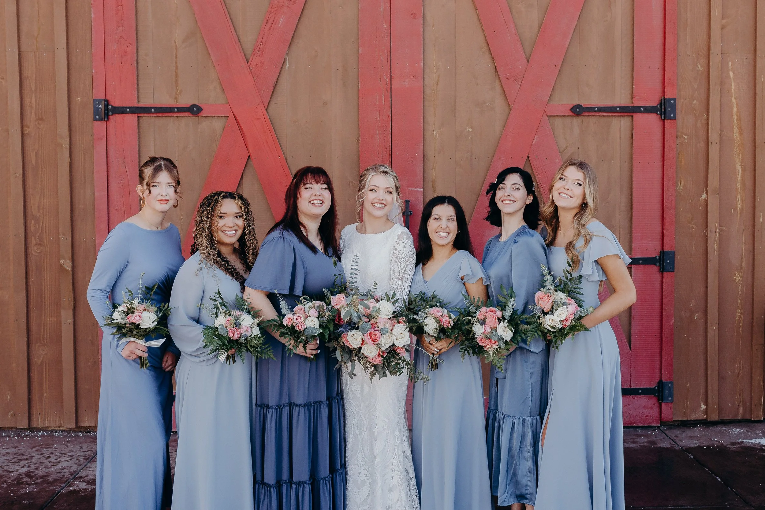 Bridesmaids holding their bouquets in front of barn doors, wearing blue