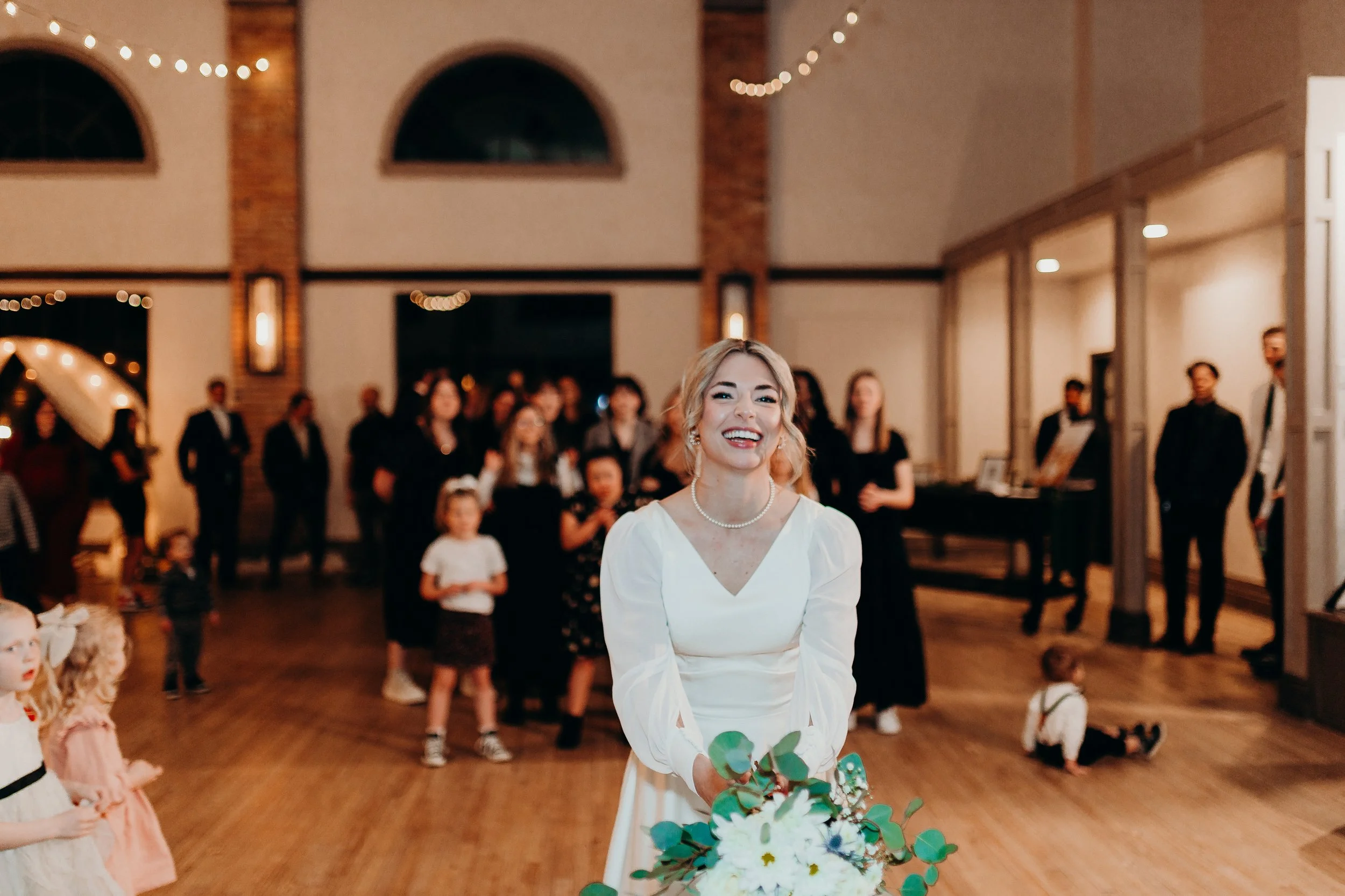 Bride tossing up bouquet to girls in black dresses in the background