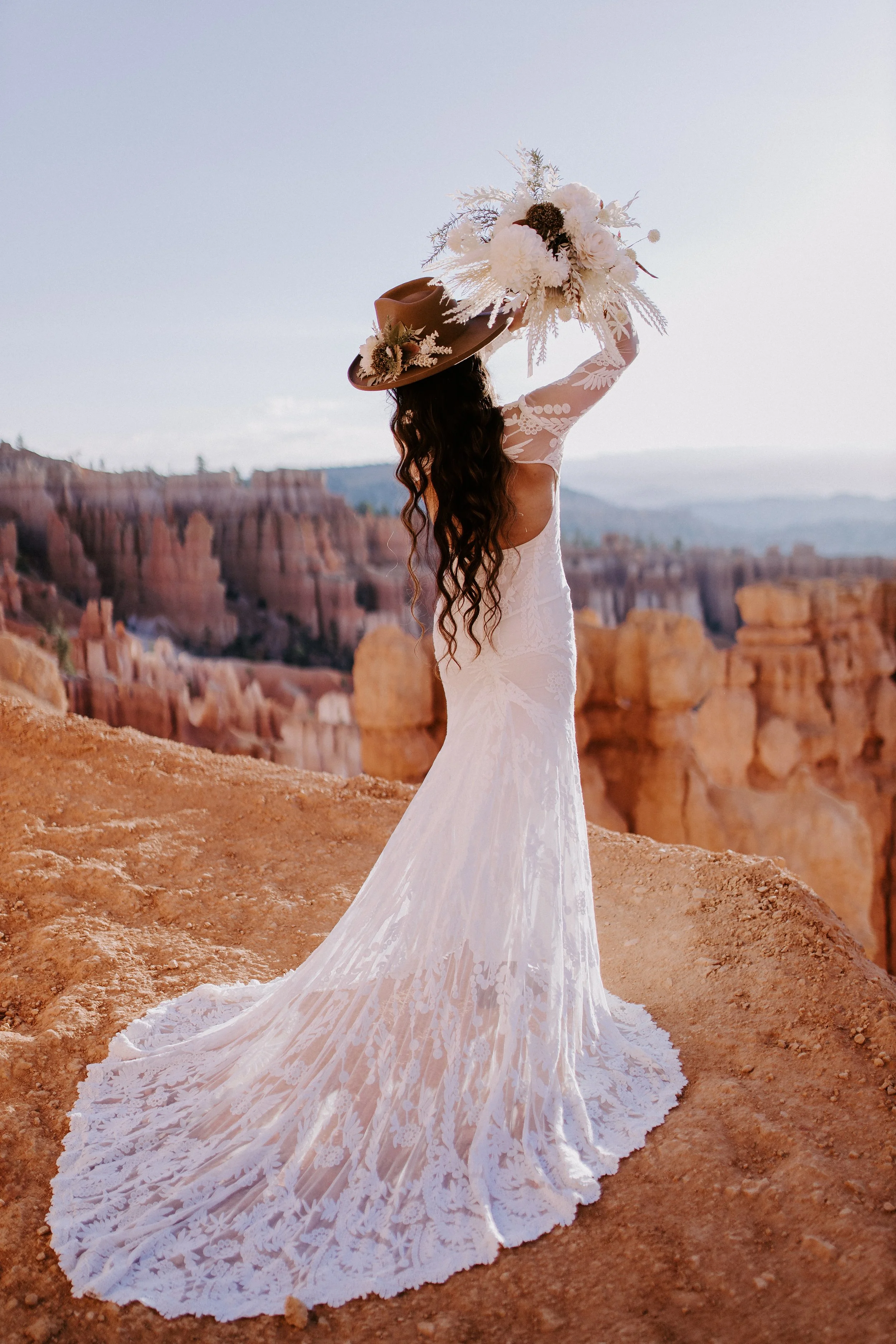 A bride in a cowgirl hat looking out at hoodoos and mountains in the background