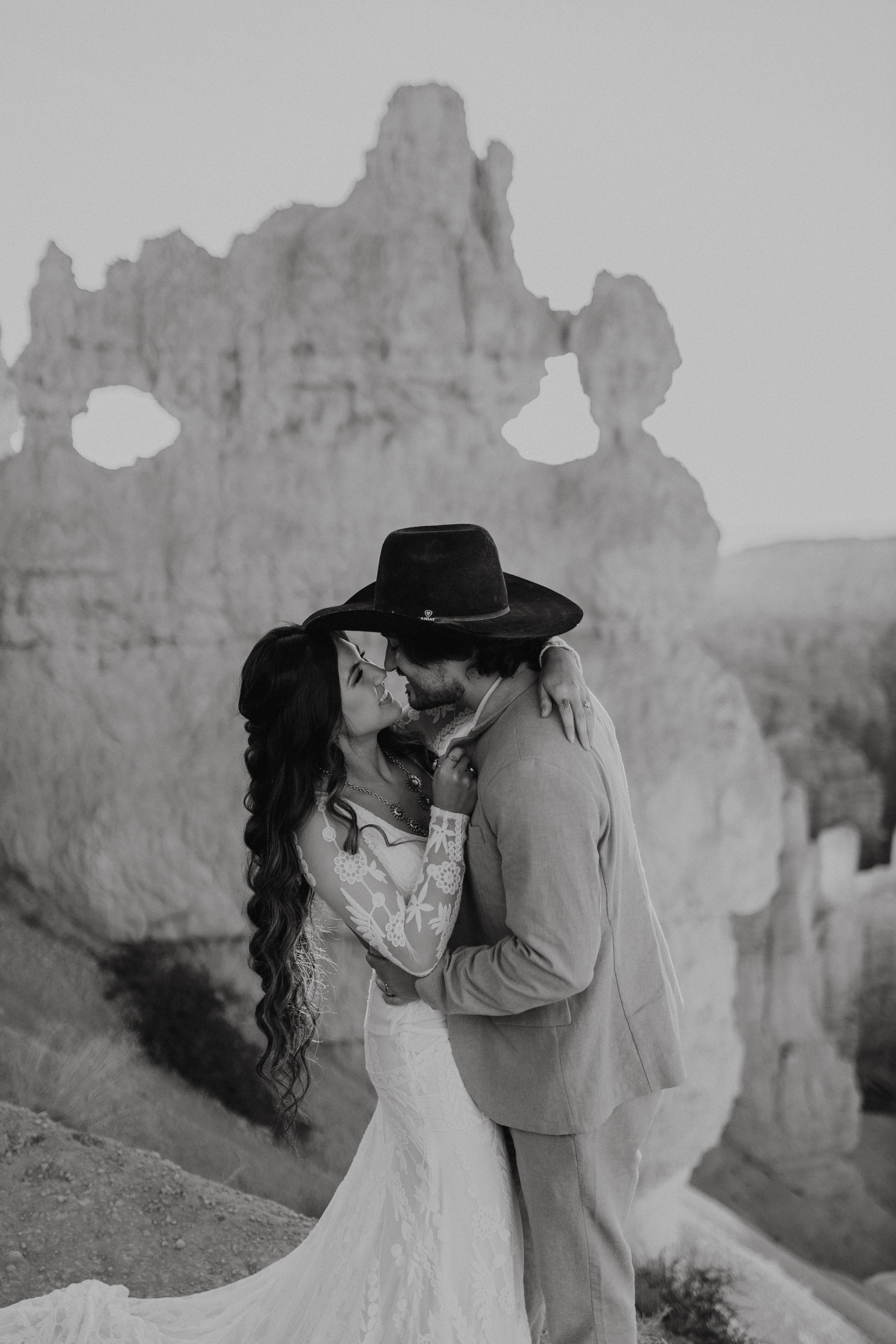 A bride and groom standing and holding each other with red rock in the background