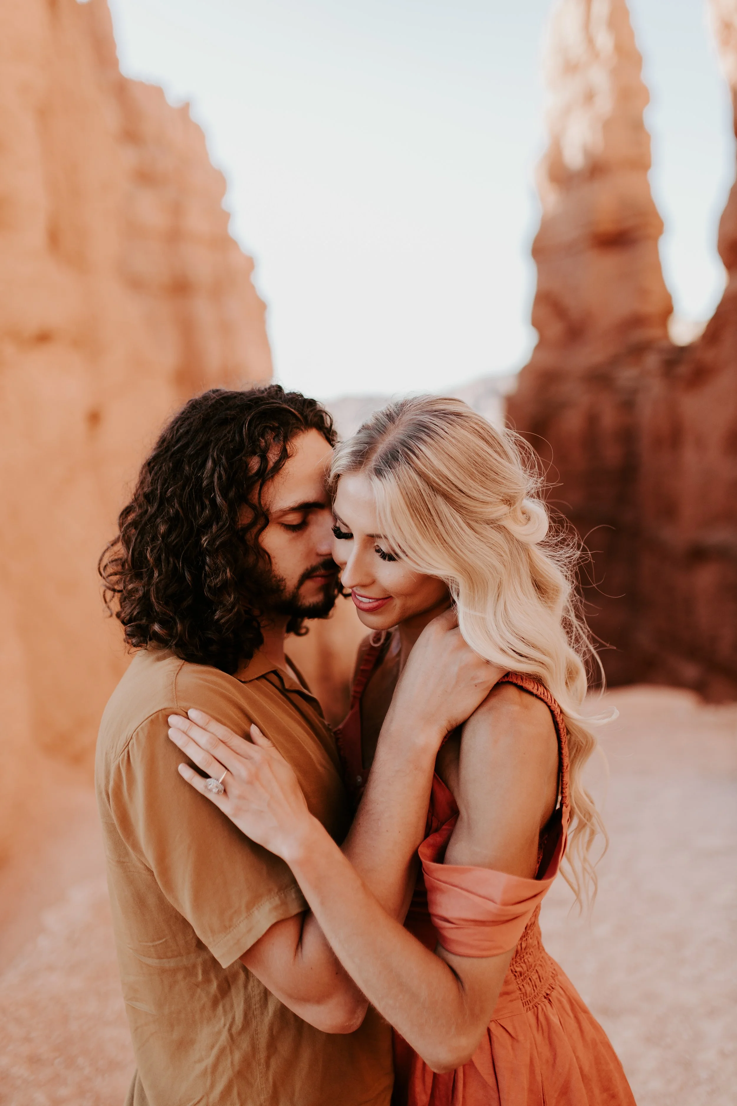 A man and woman holding each other face to face with red rock in the background
