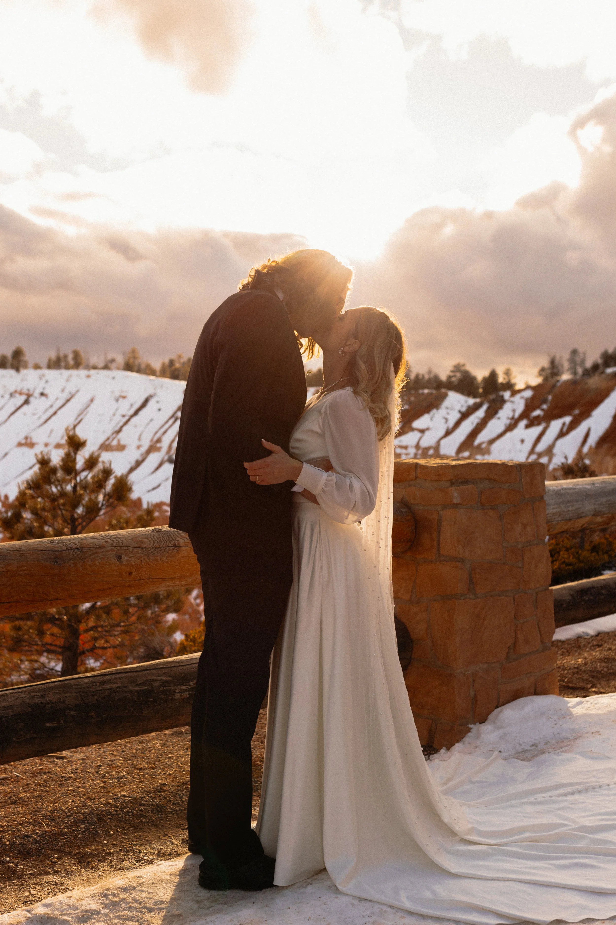 A bride and groom kissing with red rock and a sunset in the background