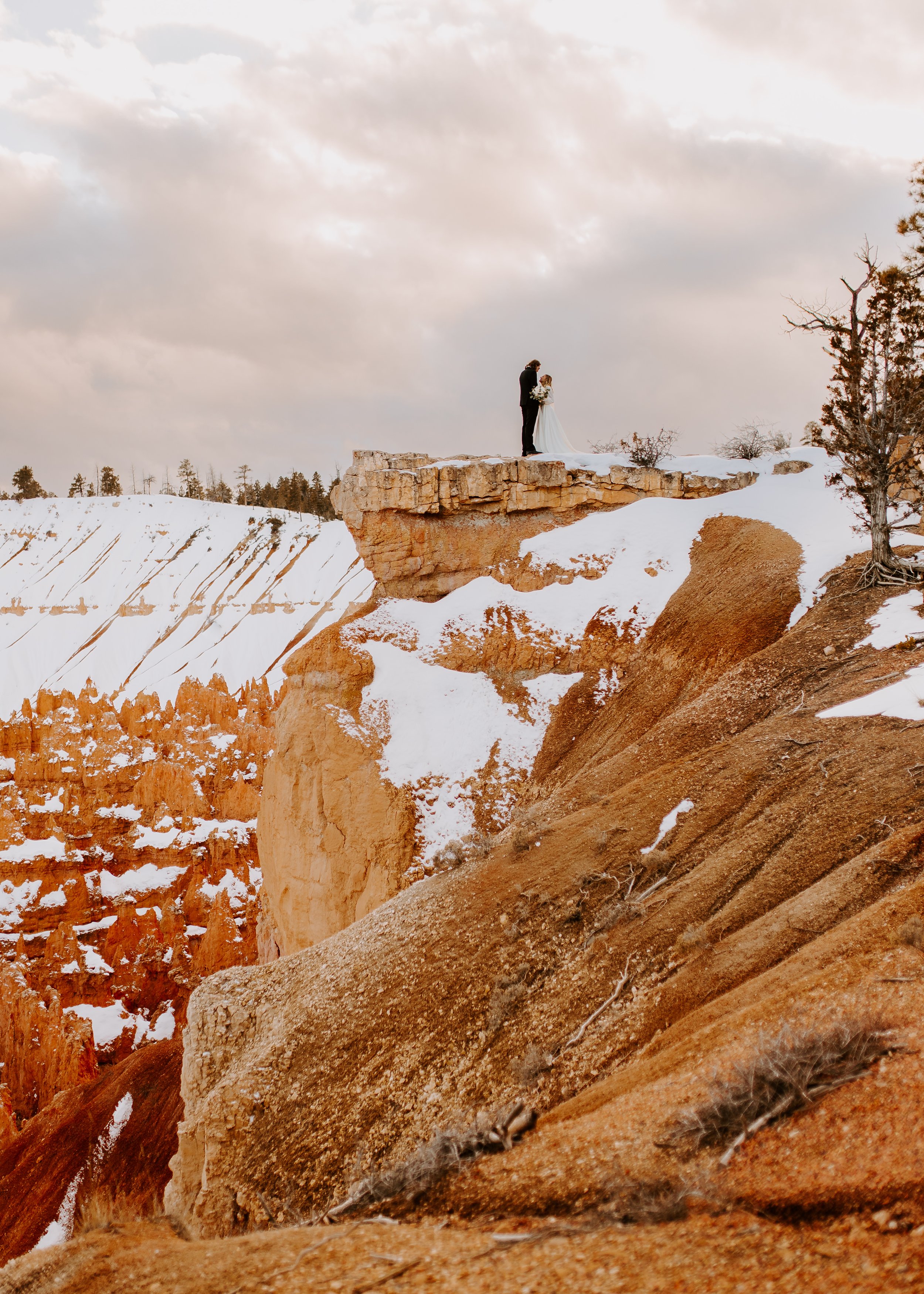 Distant shot of a bride and groom standing near a cliff with red rock in the background