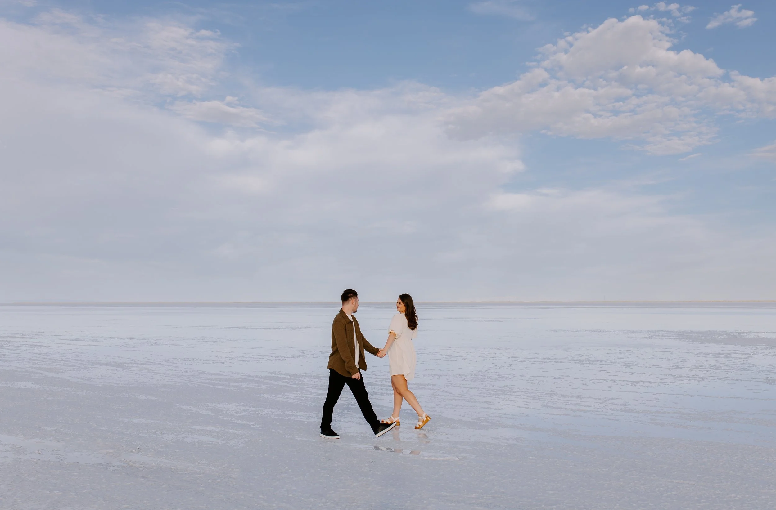 Couple holding hands on salt flats with blue cloudy skies in the background