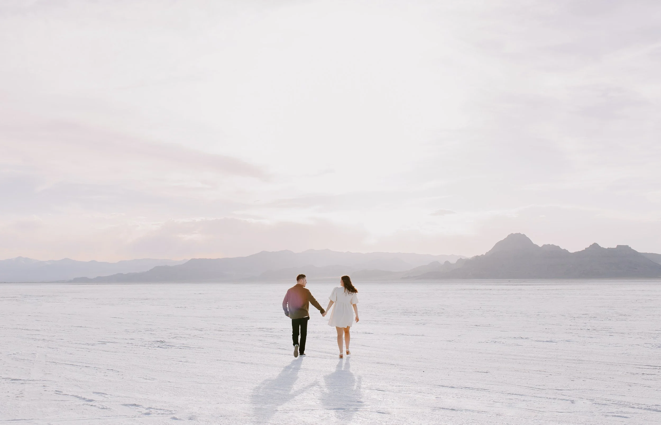 Couple walking on salt flats towards the mountains hand in hand