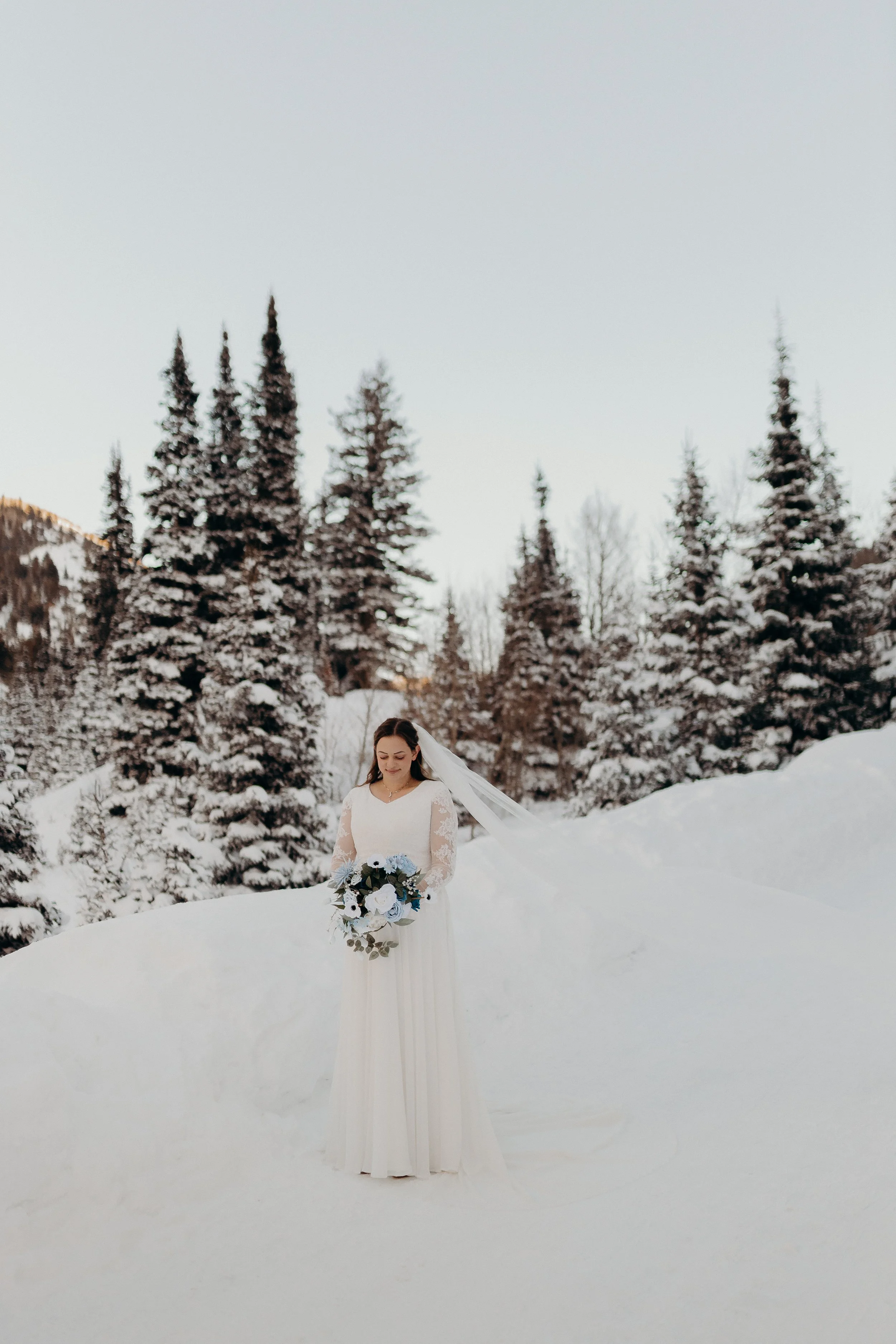 A bride holding flowers standing in snow with snowy trees in the background