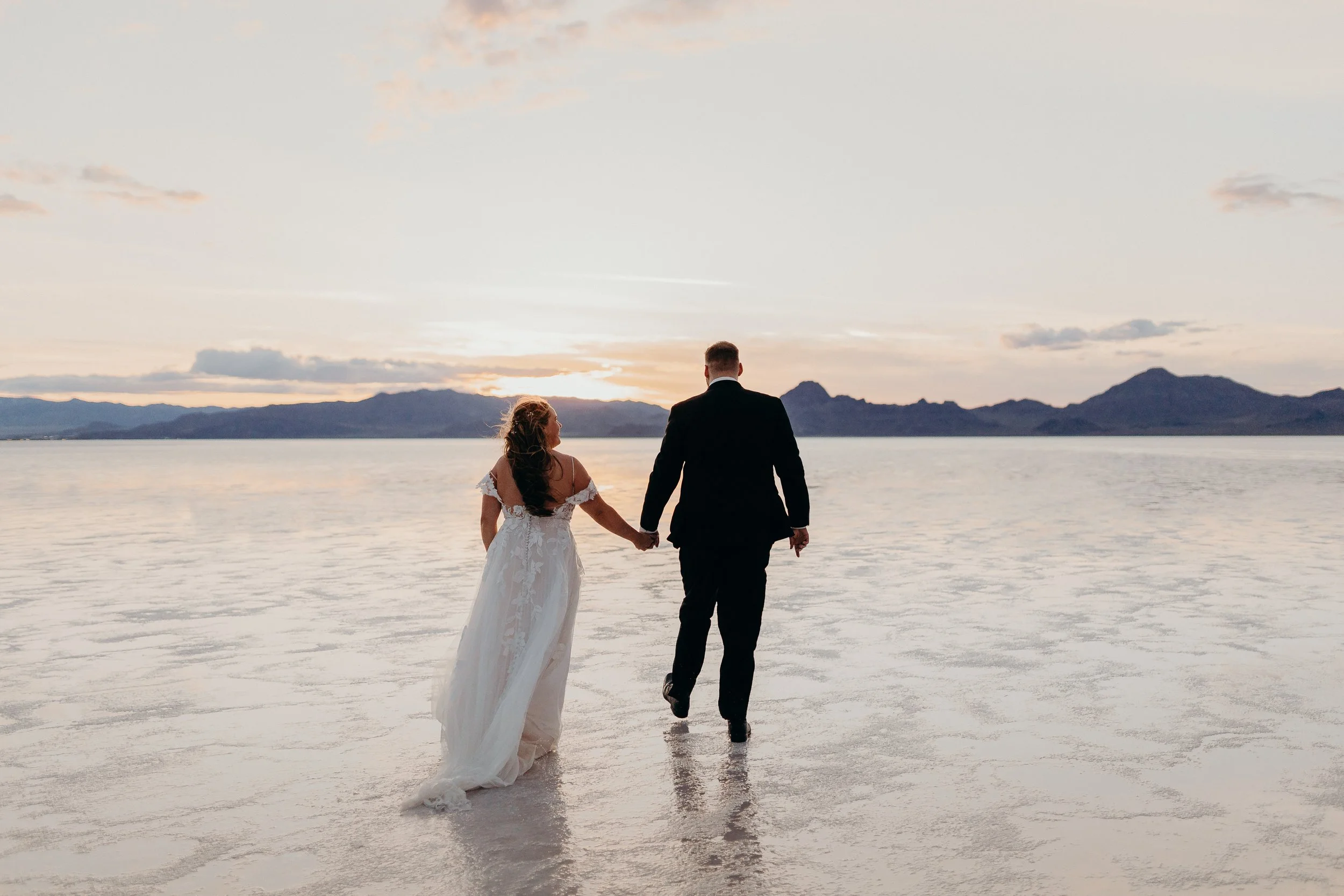 Bride and groom walking hand in hand on the salt flats towards the mountains and sunset