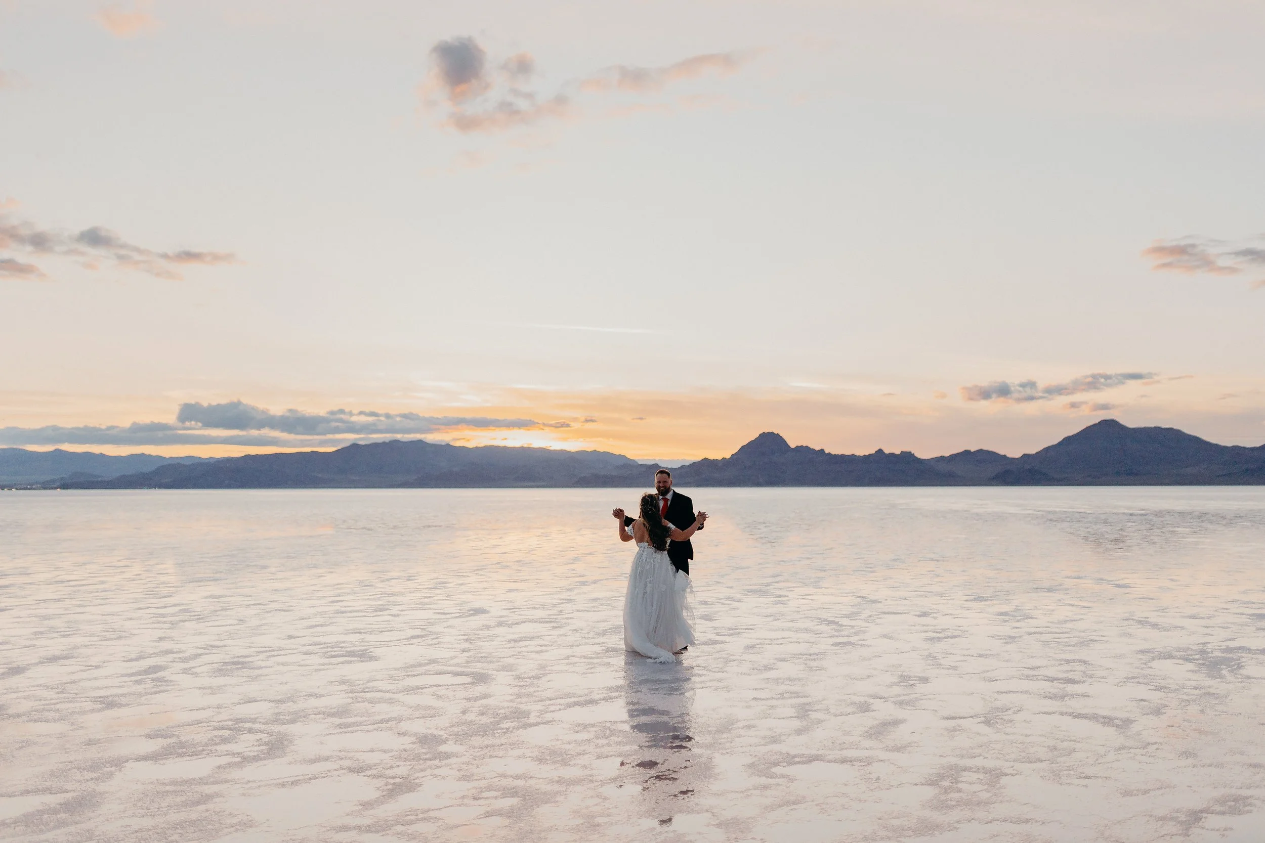 Bride and groom dancing on the salt flats with mountains and sunset in the background