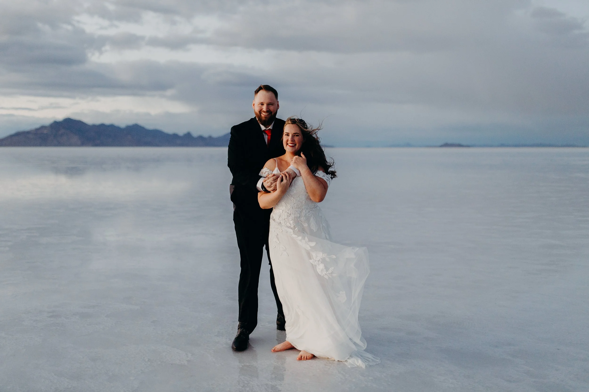 Bride and groom smiling on the salt flats with mountains and notes of blue in the background