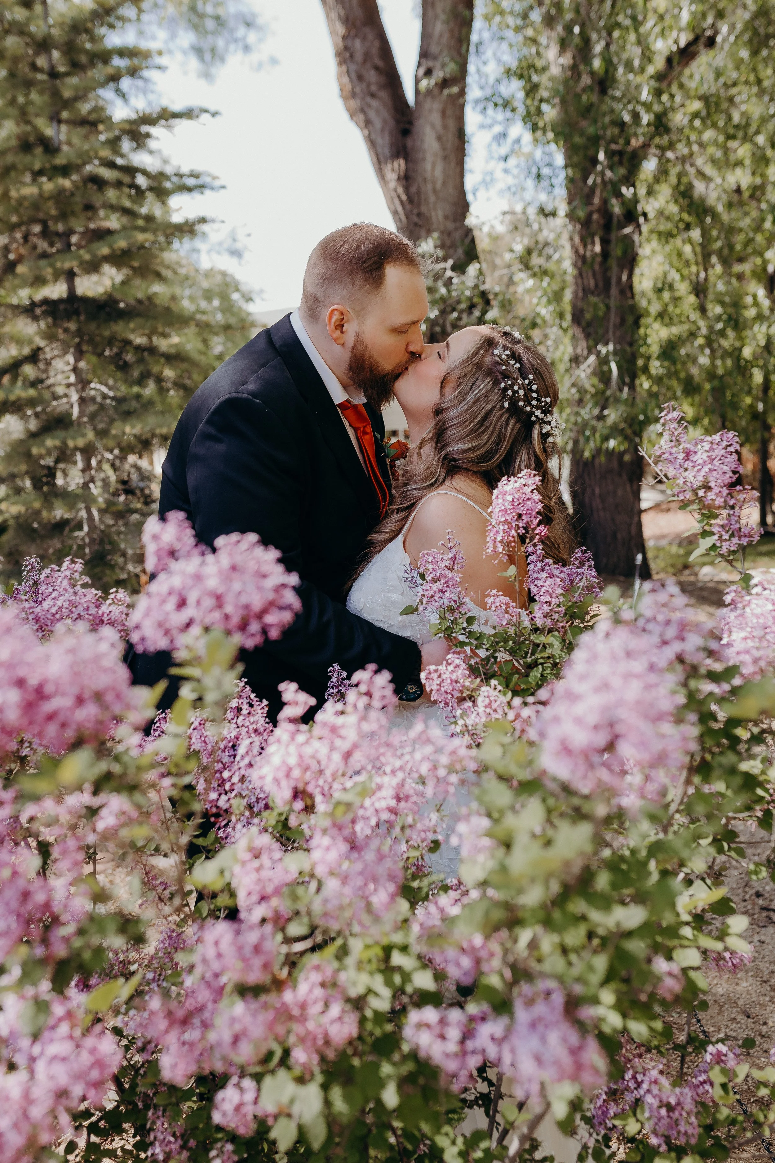 Bride and groom kissing behind a bush of purple flowers in the foreground