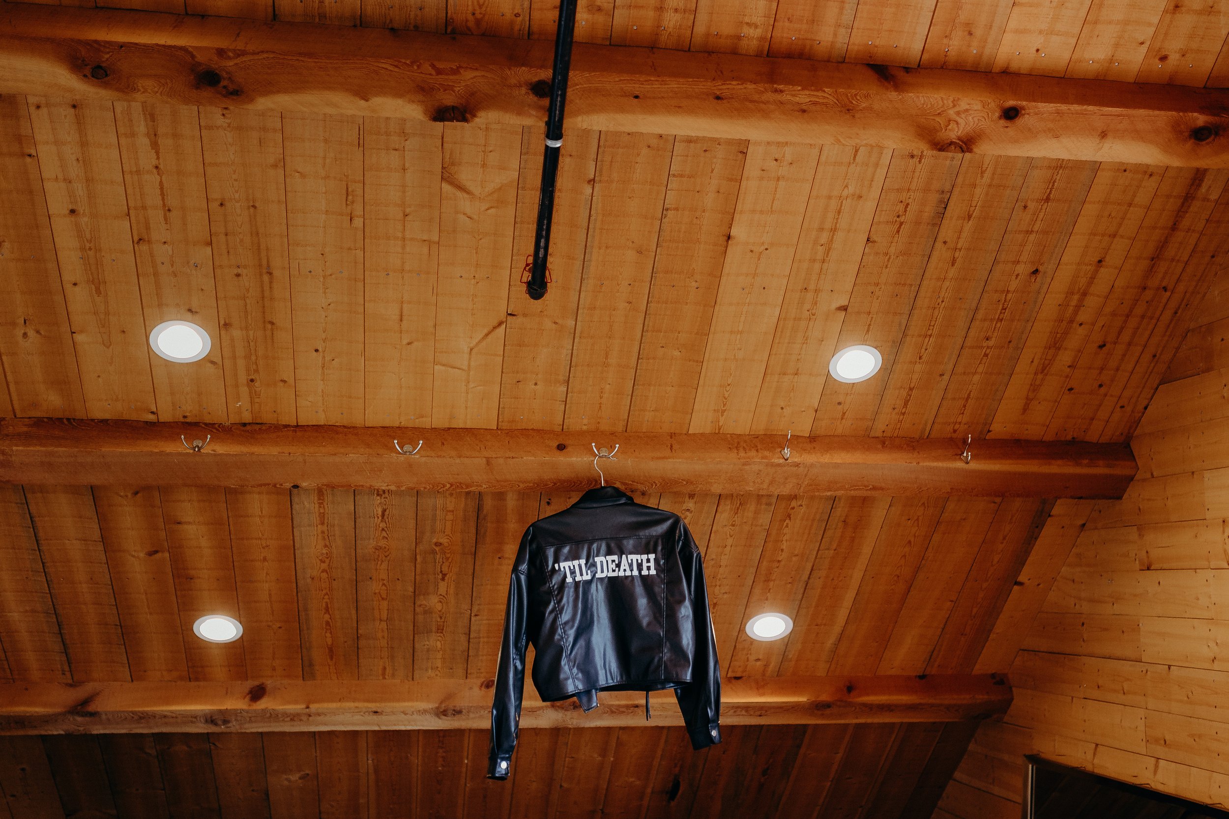 "til death" leather jacket hanging on wooden ceiling beam