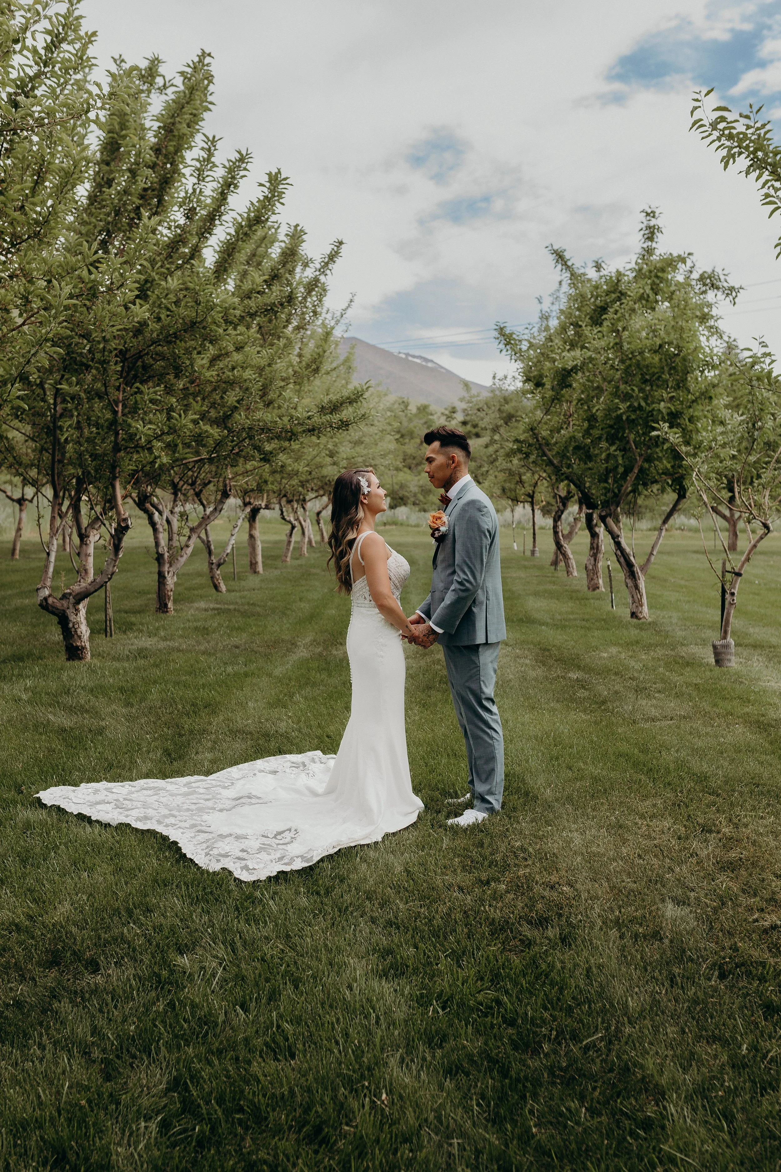 Bride and groom holding hands in a green apple orchard and looking at one another