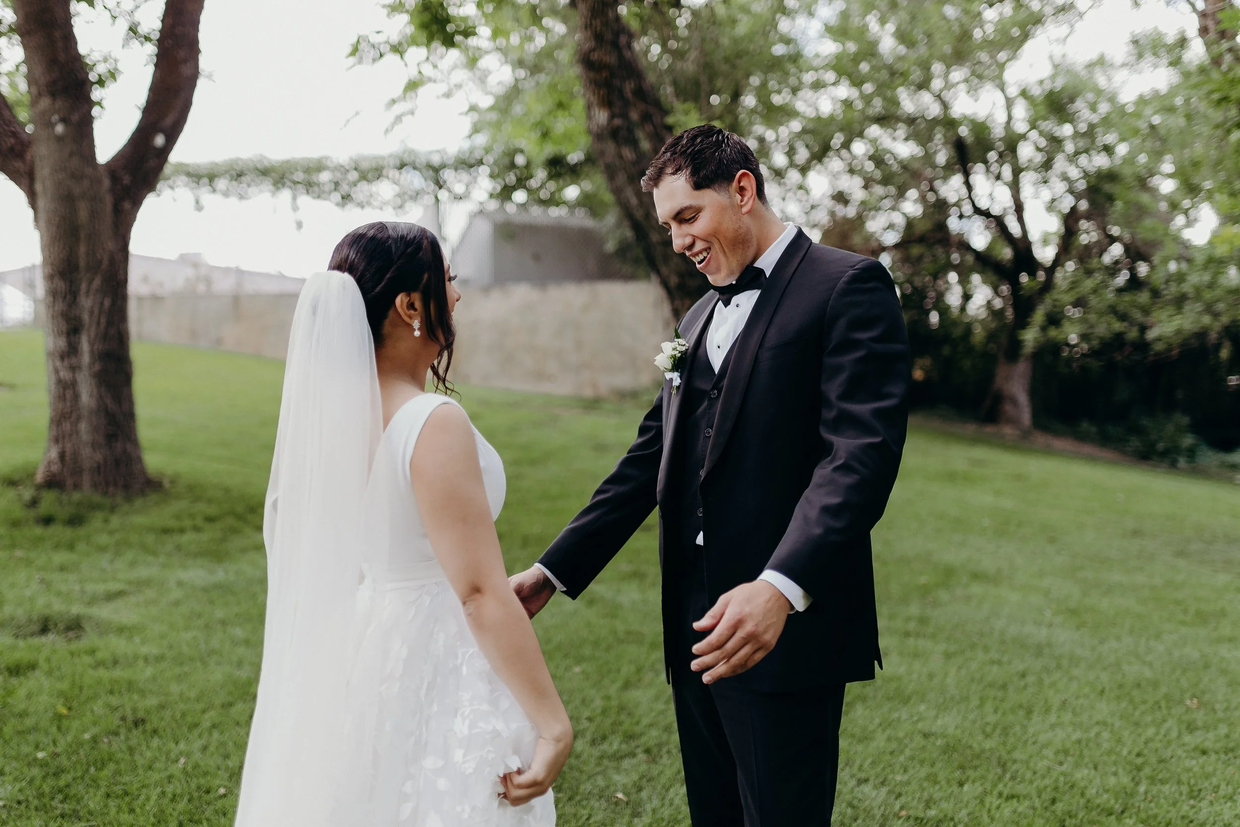 Groom seeing bride for the first time and smiling really big in a green field with green trees in the background. 
