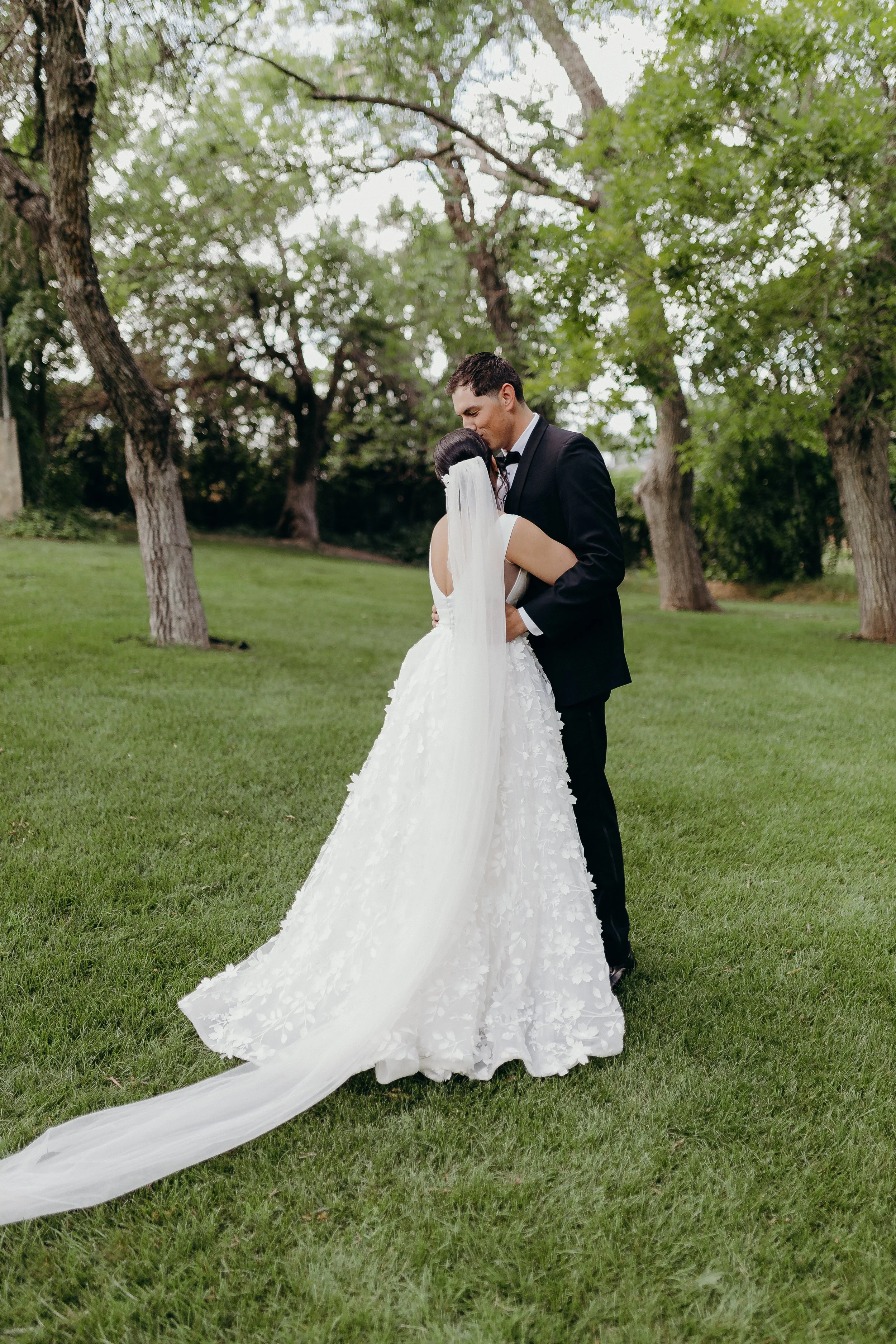 Bride hugging groom in front of green field and green trees