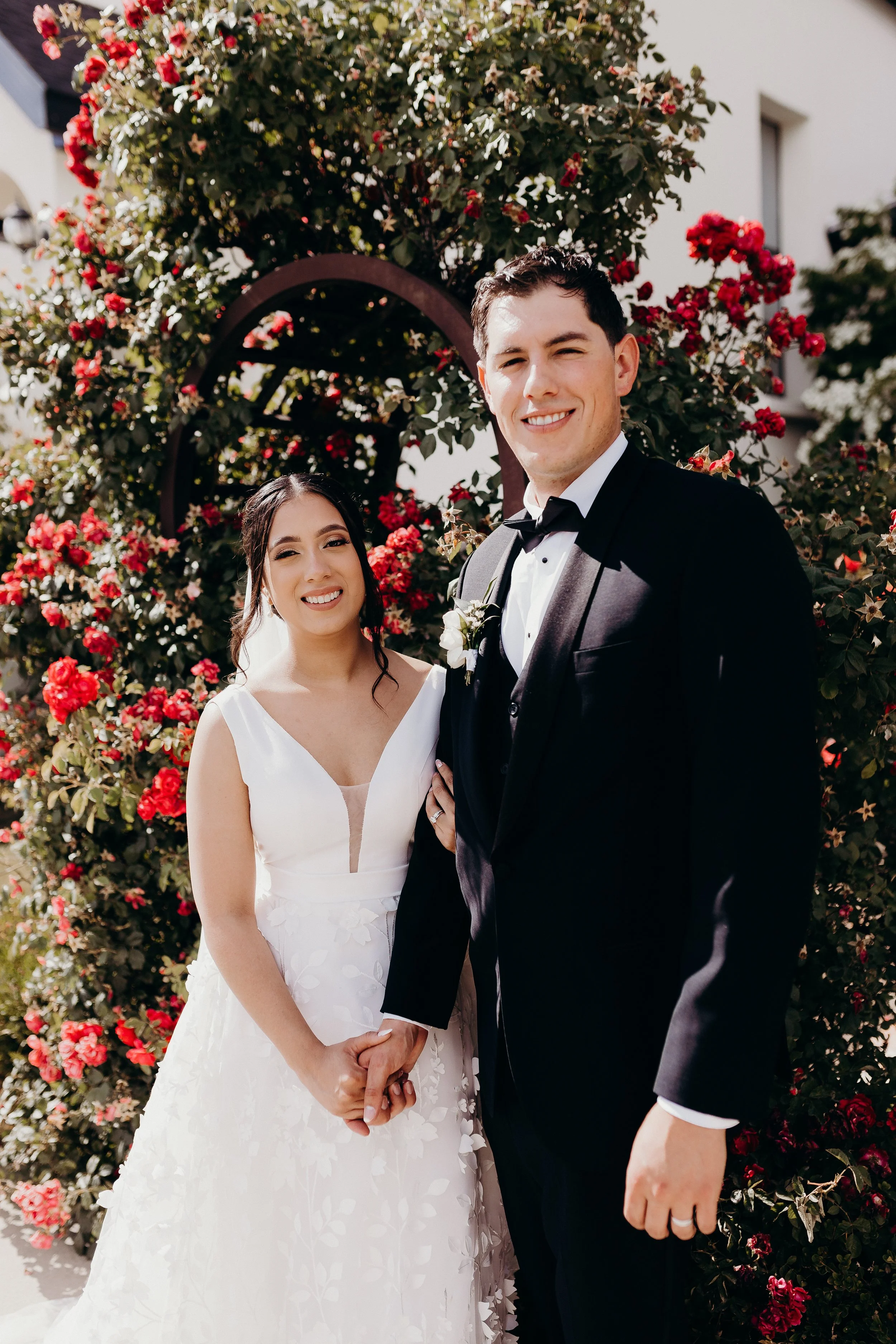 Bride and groom smiling in front of roses and garden arch