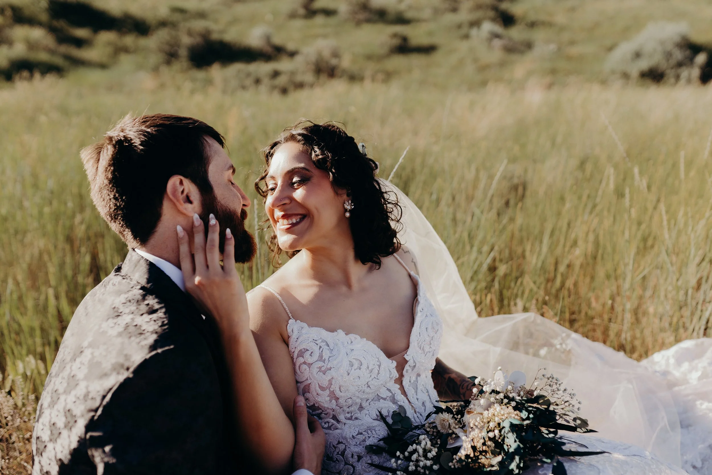 Bride looking at groom and smiling in field of grass