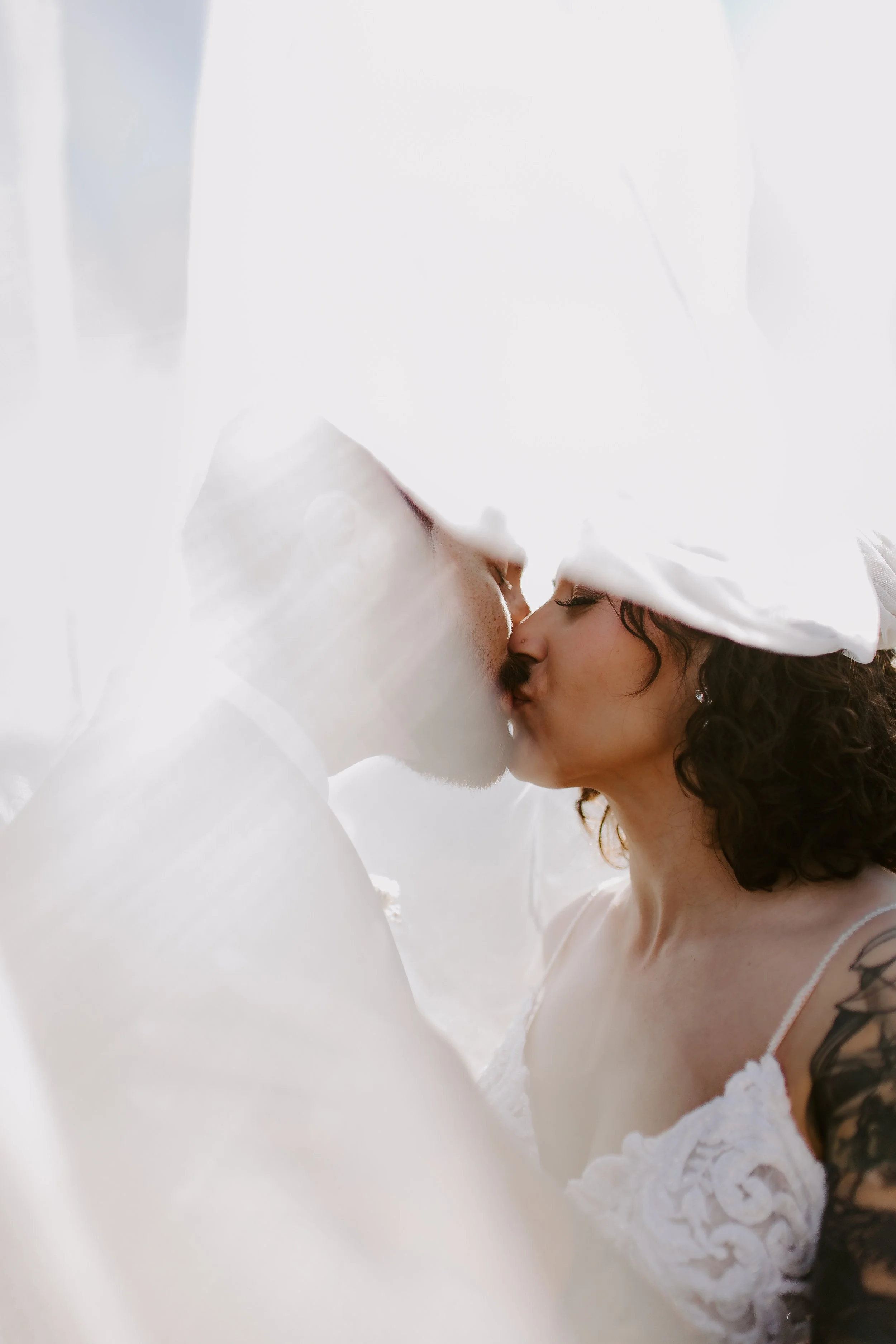 Bride and groom kissing underneath veil