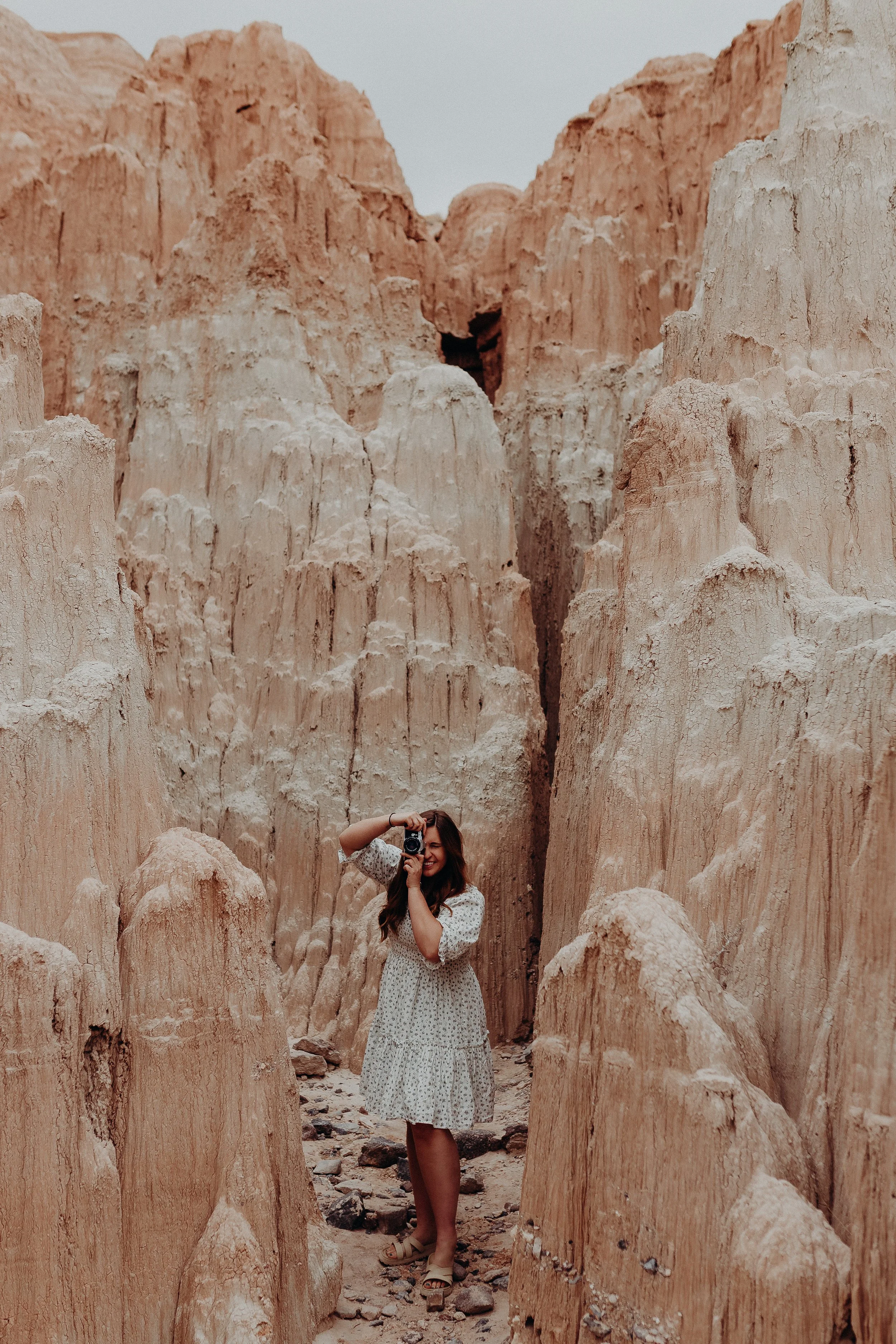 Woman in white dress taking a picture in front of rock formations
