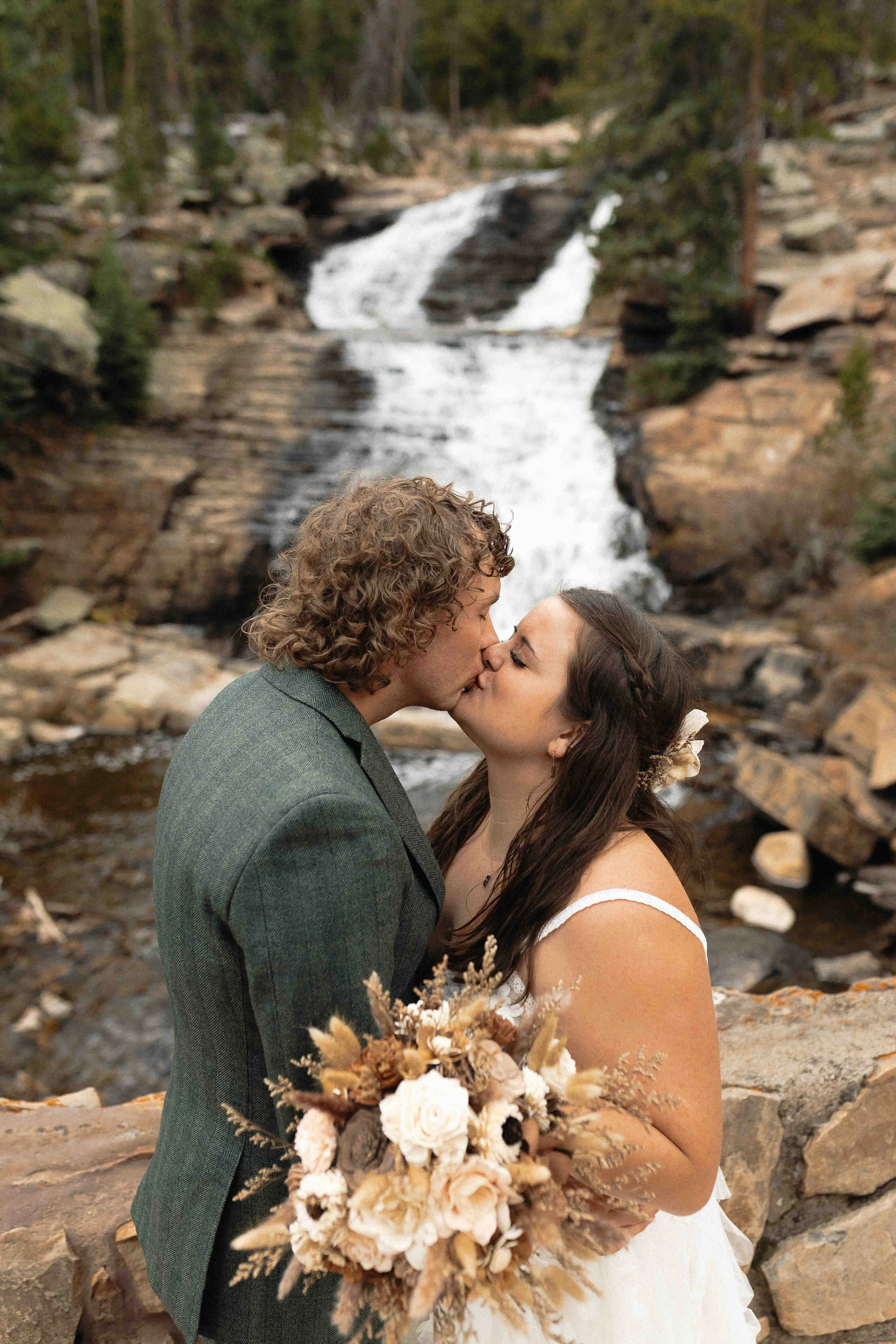 a bride and groom kissing in front of a waterfall.