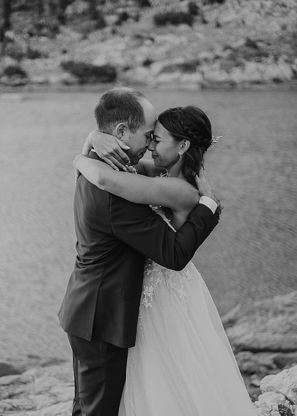 black and white photo of bride and groom embracing in front of a lake