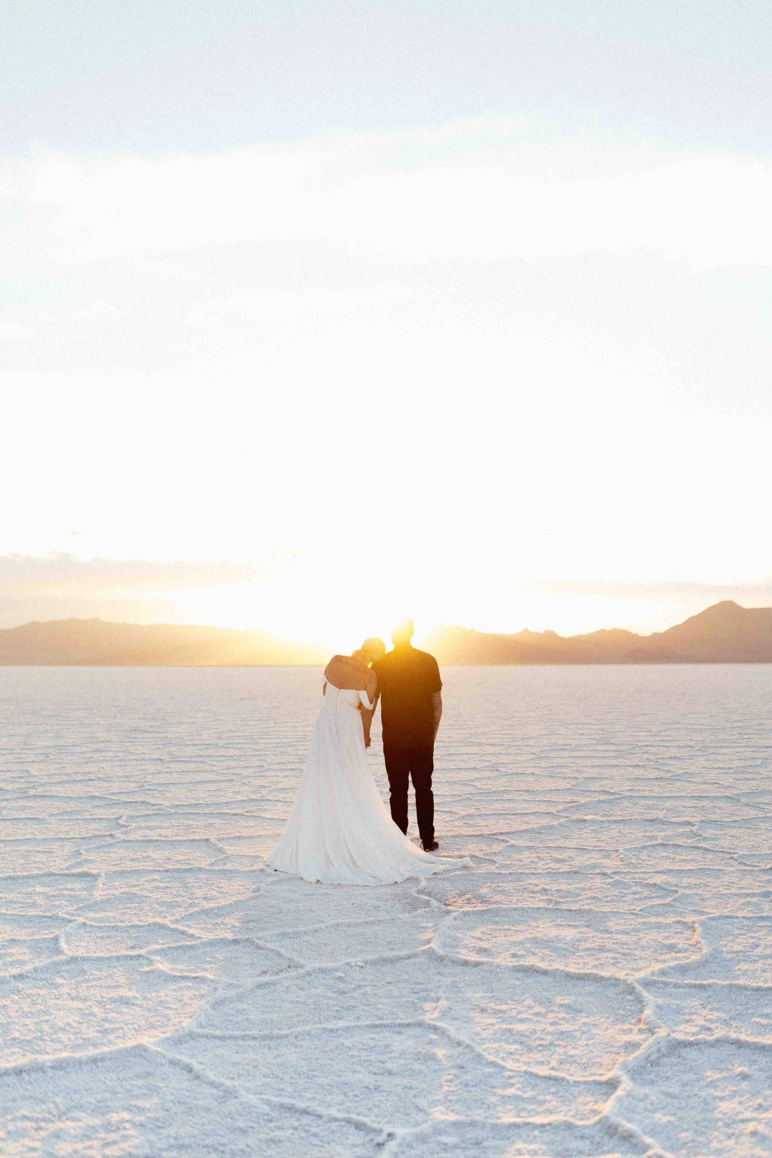 Bride and groom gazing upon the sunset with mountains in the background of the bonneville salt flats.