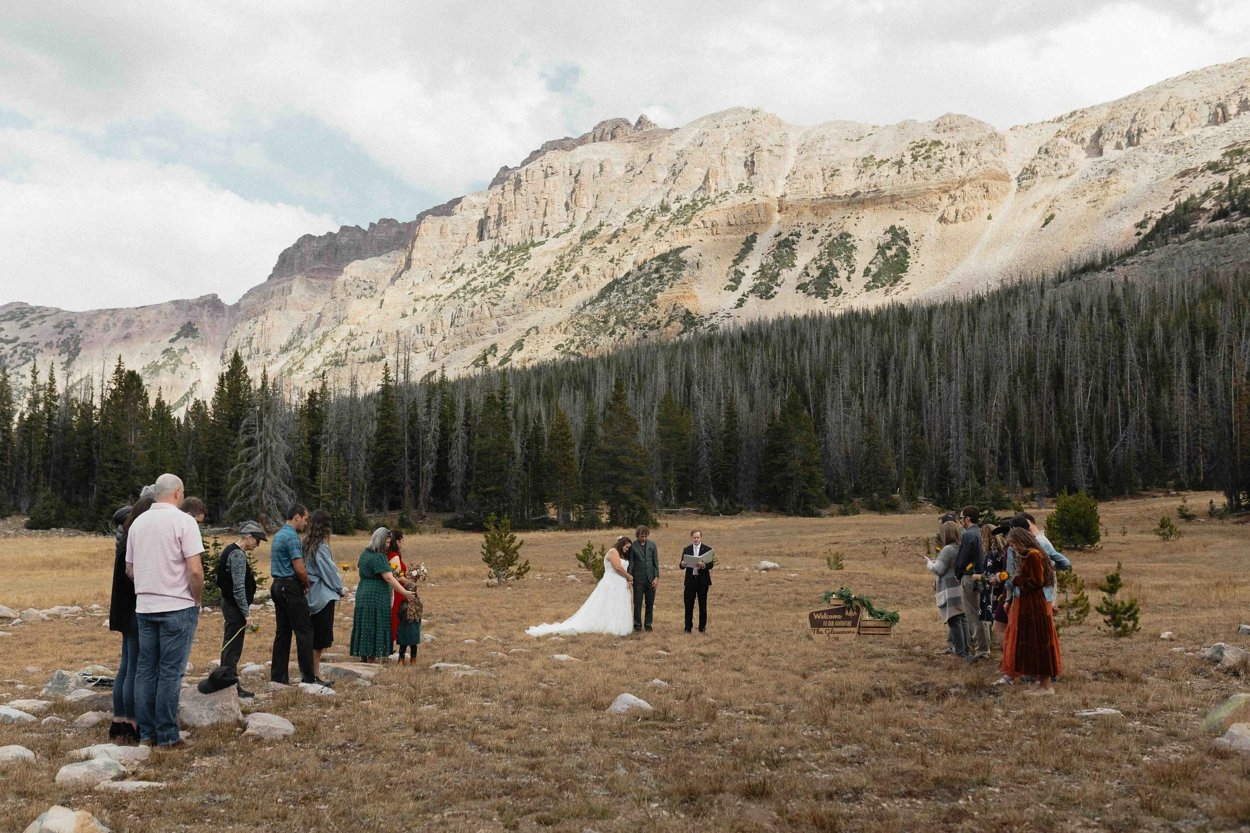 A bride, groom, and officiant plus about 20 guests, standing in front of the mountains of Utah for a marriage ceremony.