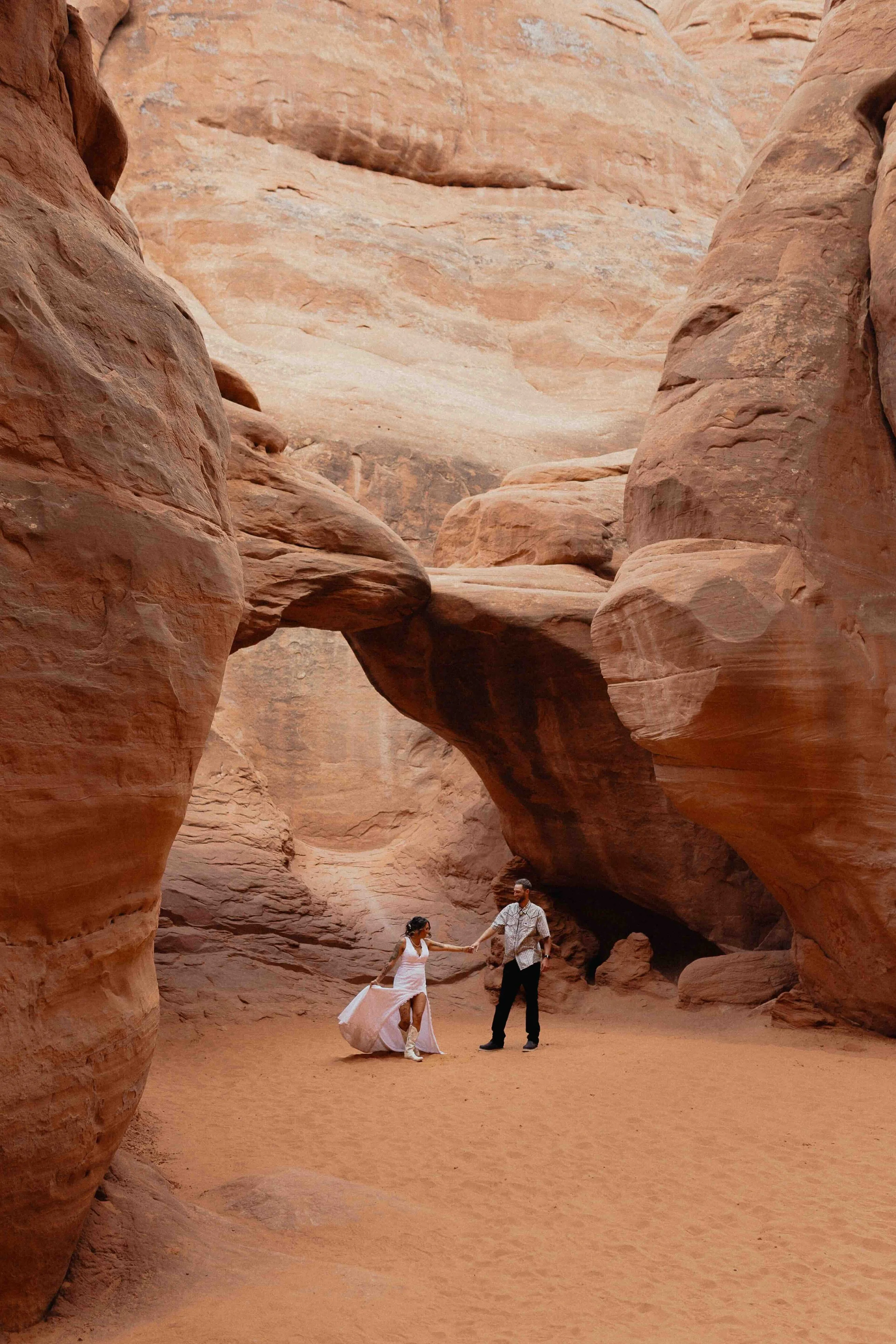 bride and groom dancing on sand underneath a red rock arch in Moab.