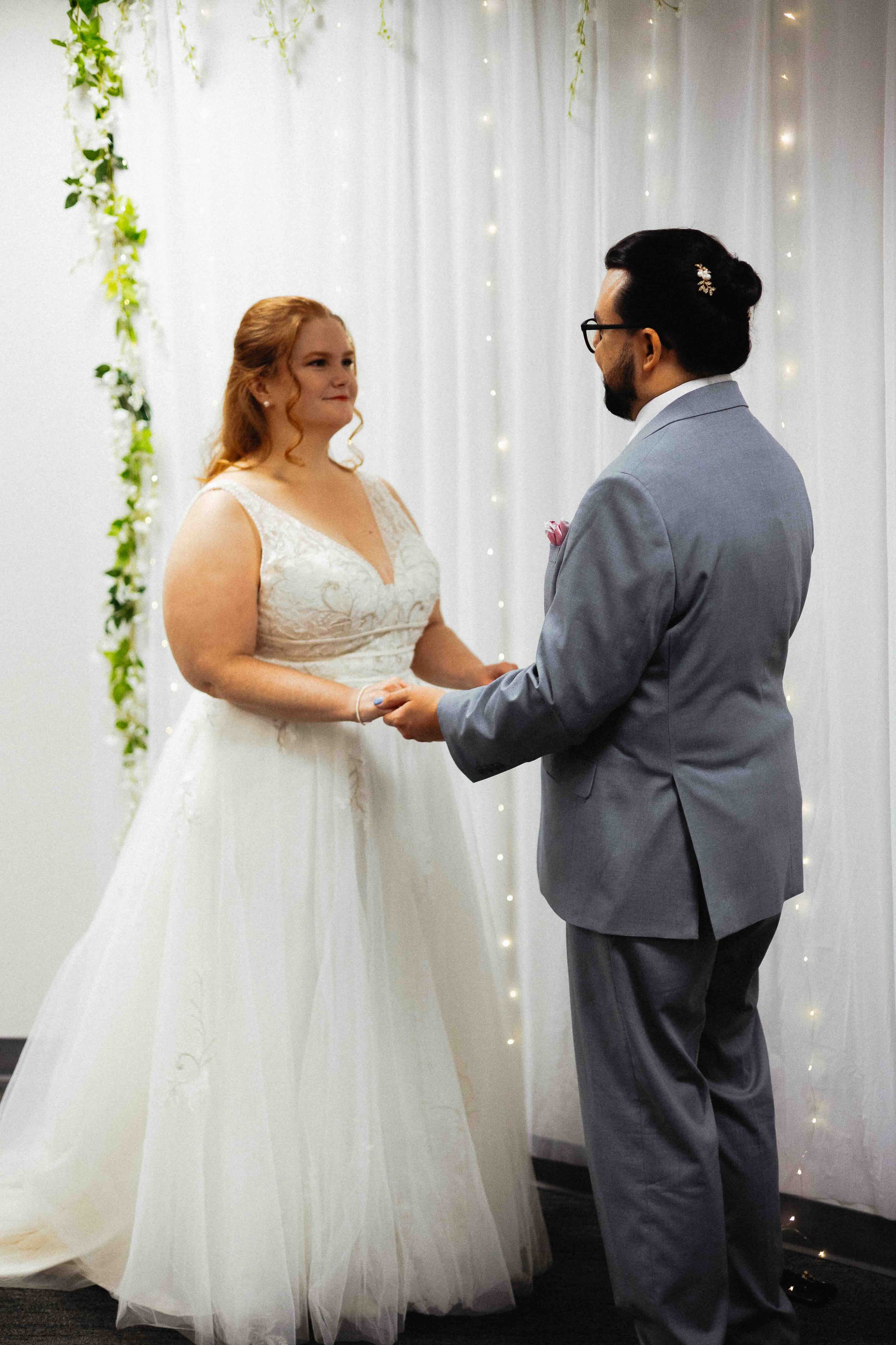 Bride and groom marrying at the SLC courthouse in front of white curtain with lights.