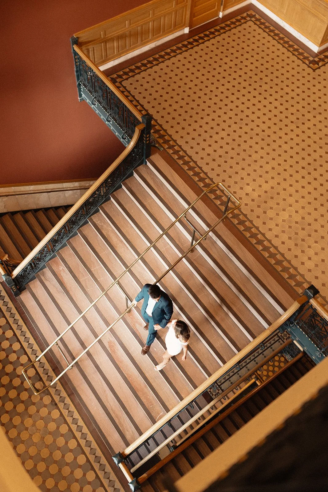 Bride and groom walking down a vintage staircase with gold tones and embellishments.